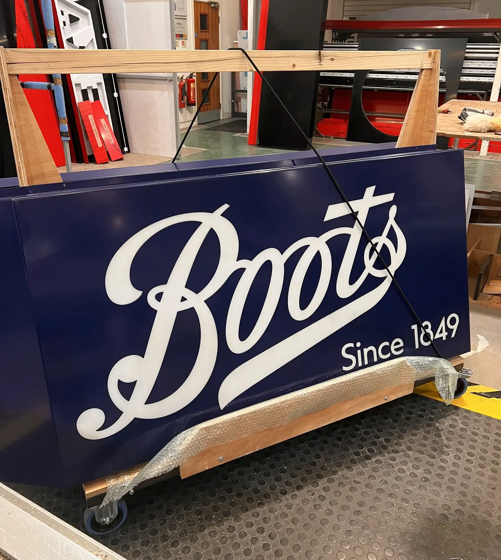 A blue sign with "Boots Since 1849" in white script, secured on a wooden frame.
