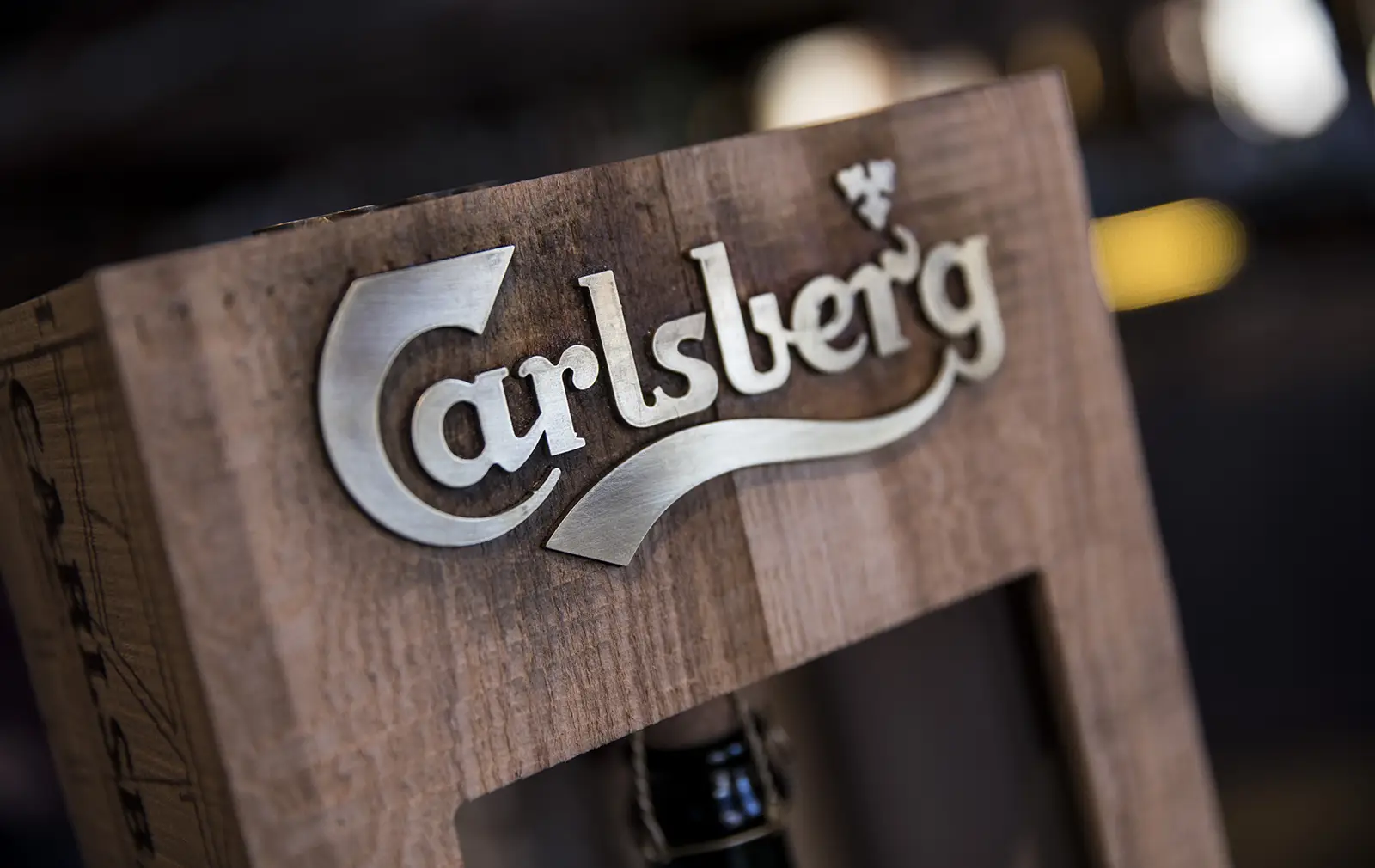 Carlsberg logo on a wooden surface with blurred background.