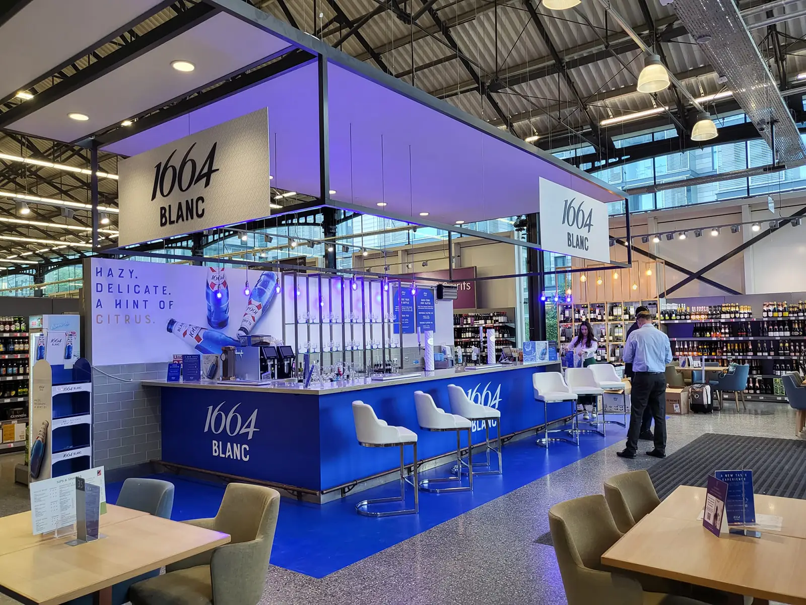 A modern bar with "1664 Blanc" branding, blue lighting, and seating in a spacious venue.