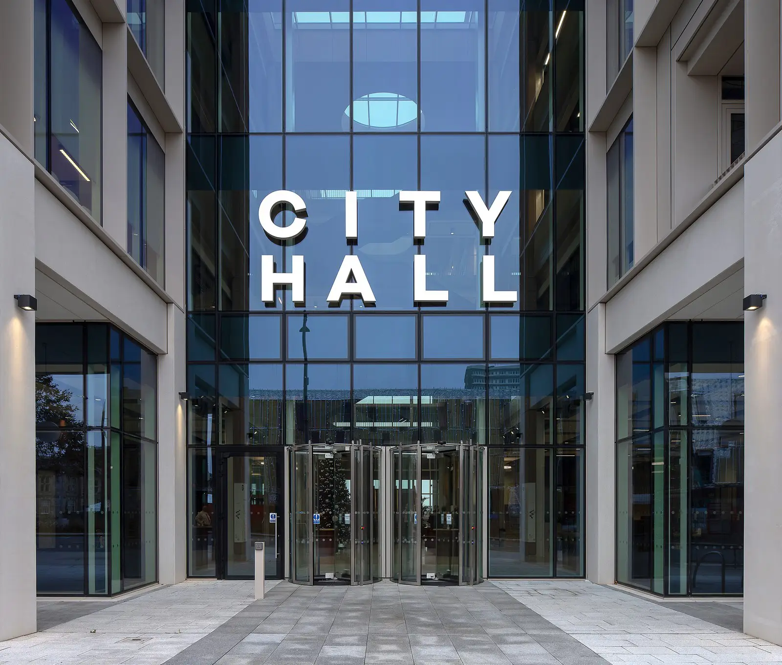 Glass entrance of a modern building with "City Hall" in large white letters above.