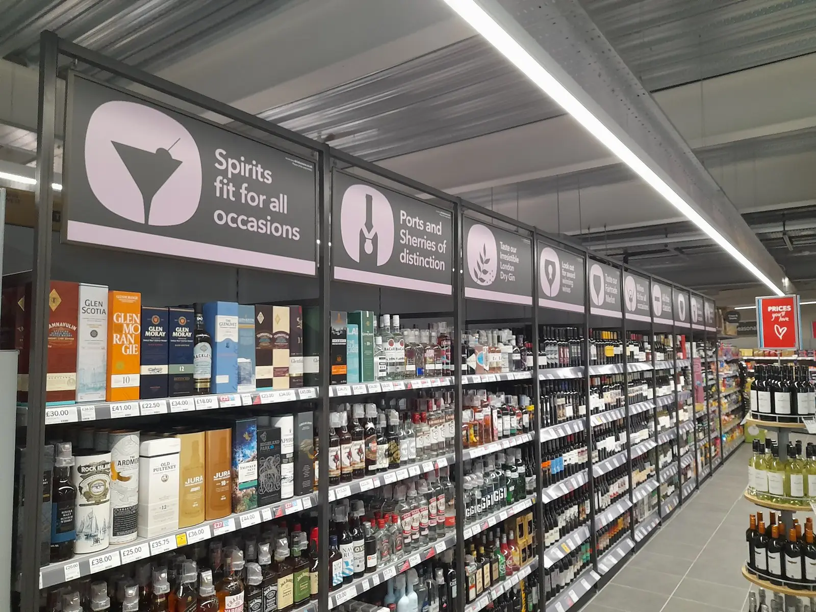 A supermarket aisle with shelves of various spirits and signs indicating different liquor categories.