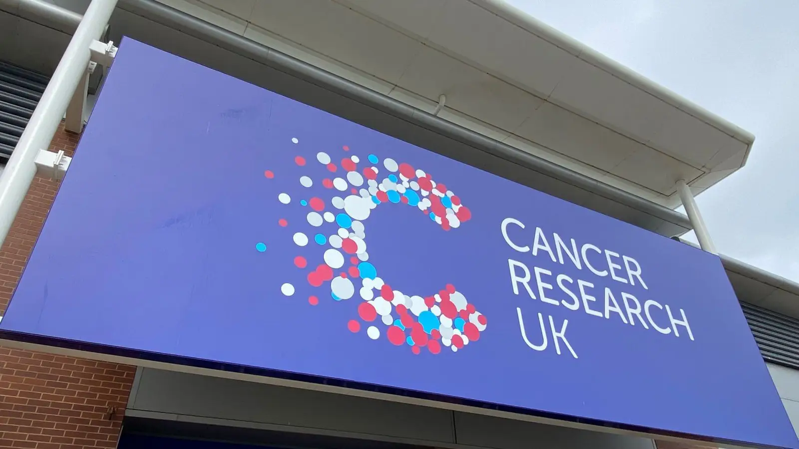 Large blue Cancer Research UK sign with a colorful circular pattern on a building.