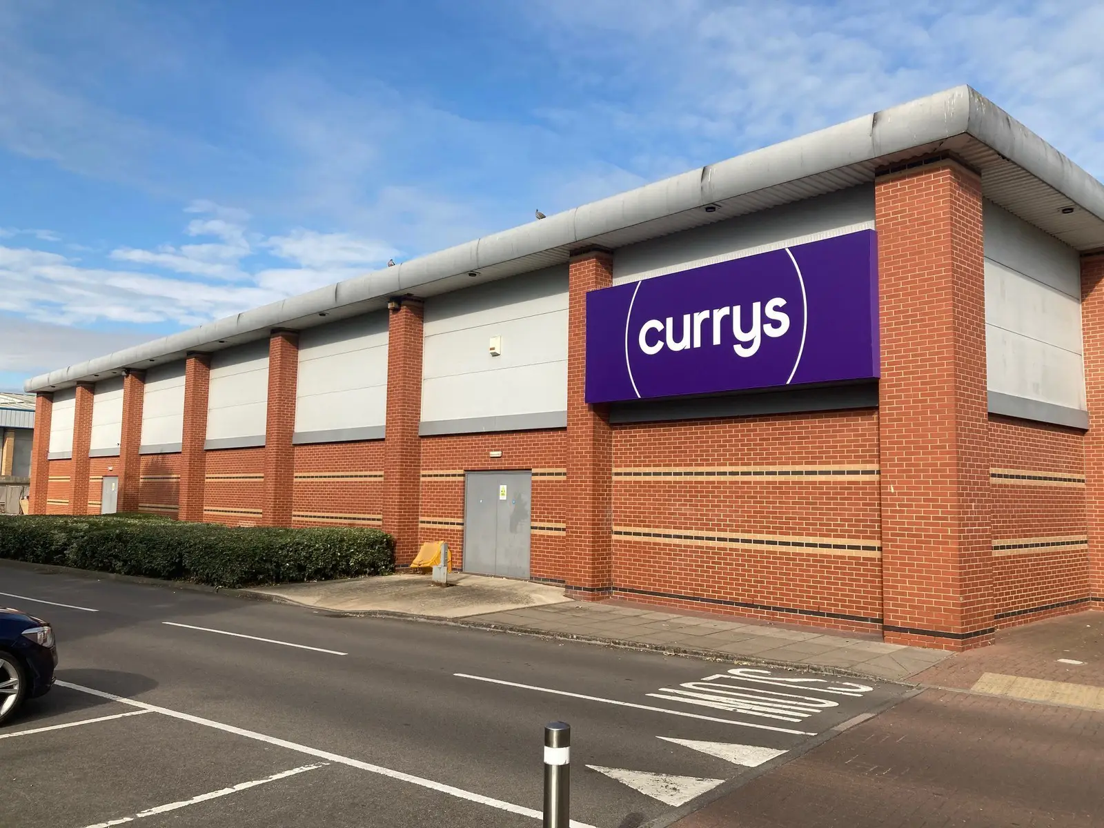 A brick building with a large purple "currys" sign and an empty parking lot.