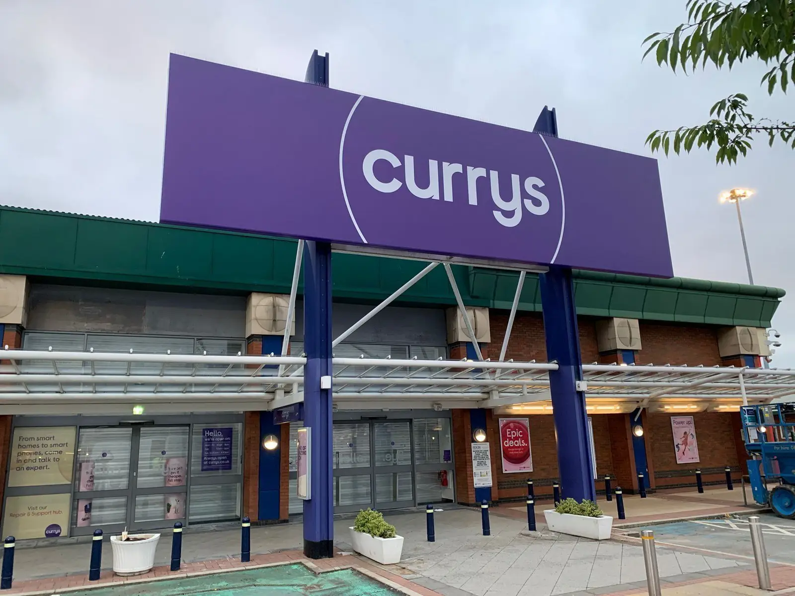 Large purple Currys sign above a closed storefront with glass doors and potted plants.