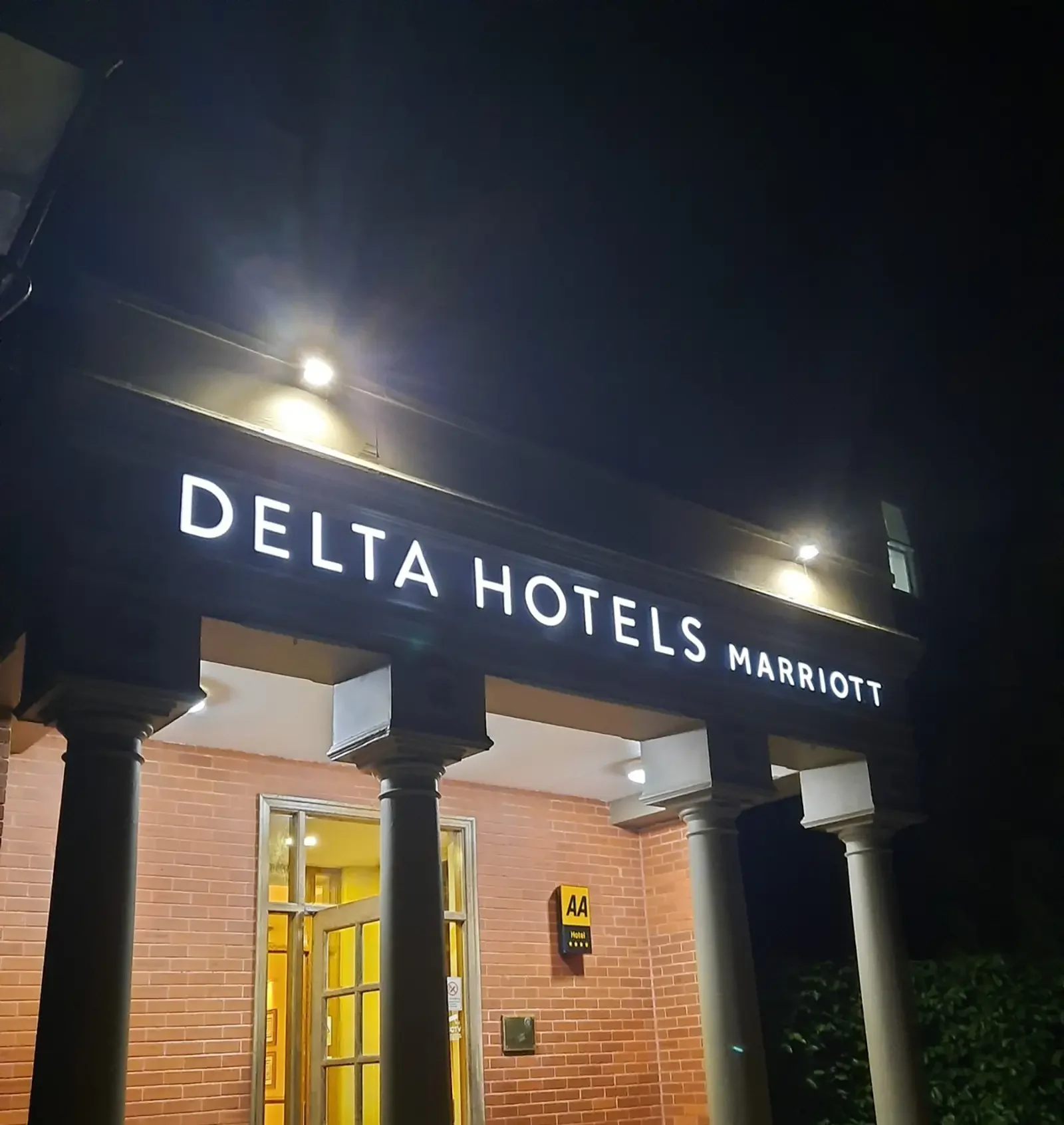 Delta Hotels Marriott entrance at night with illuminated sign and brick wall background.