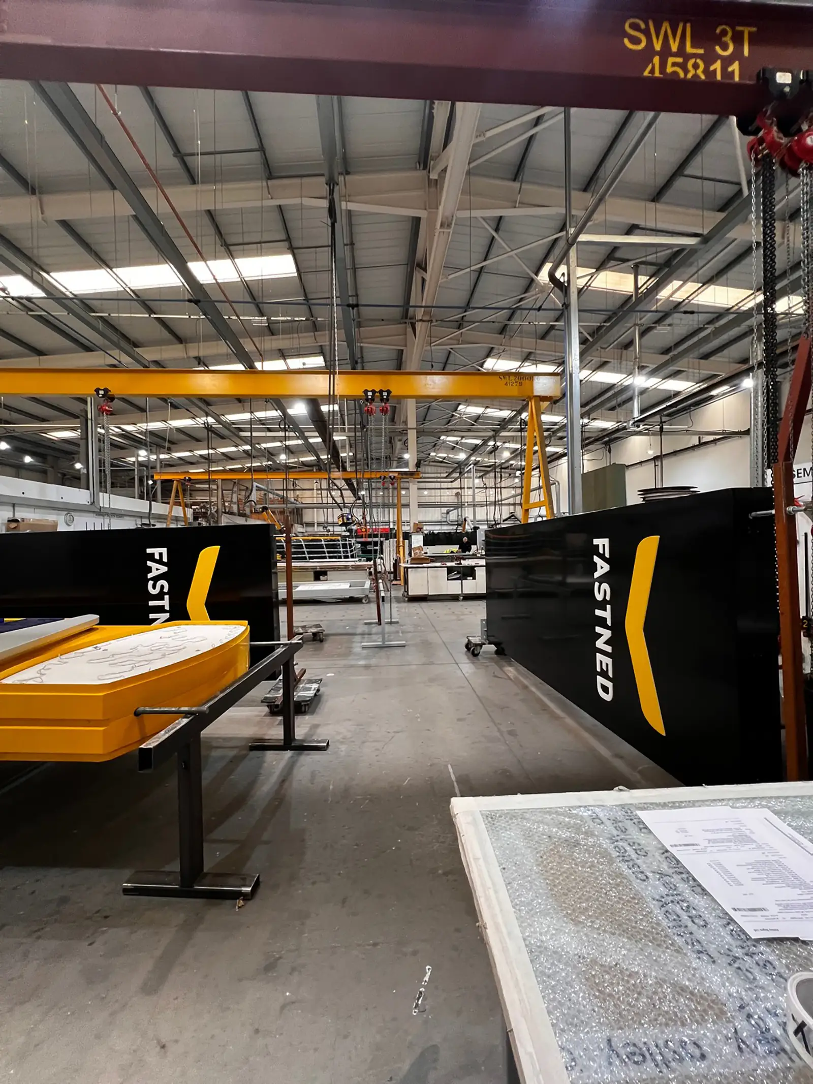 Industrial warehouse interior with large black and yellow Fastned equipment and overhead cranes.