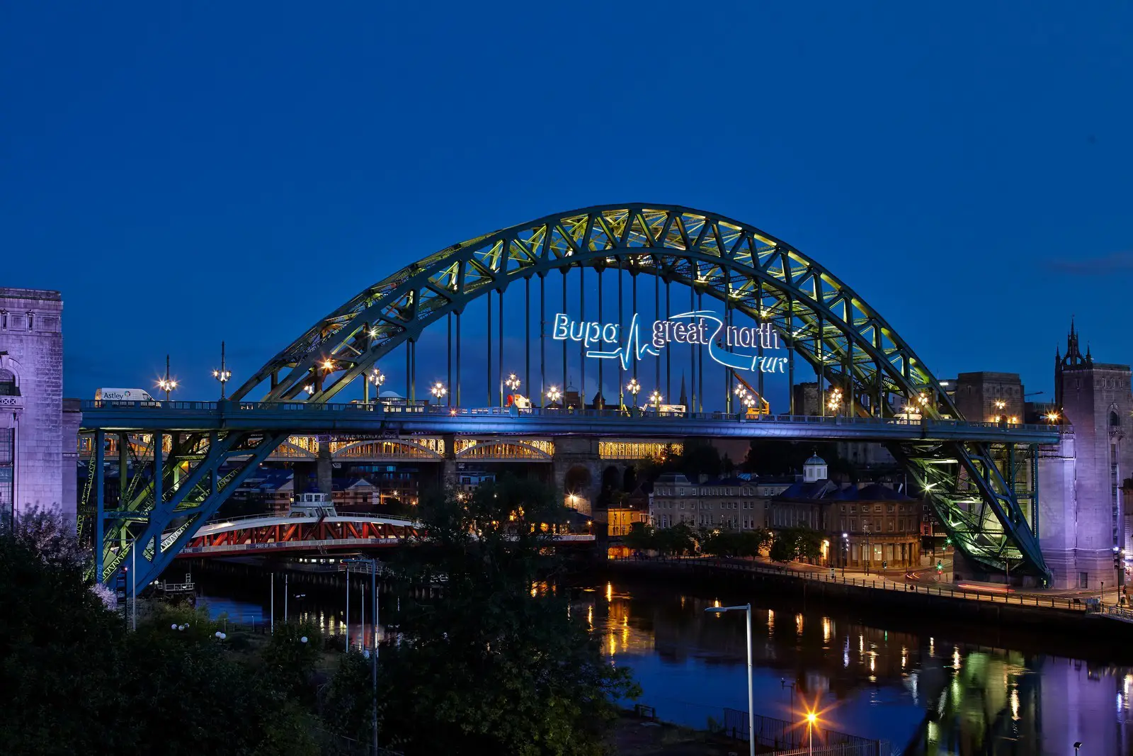 Illuminated arched bridge over a river at night with city lights and reflections.