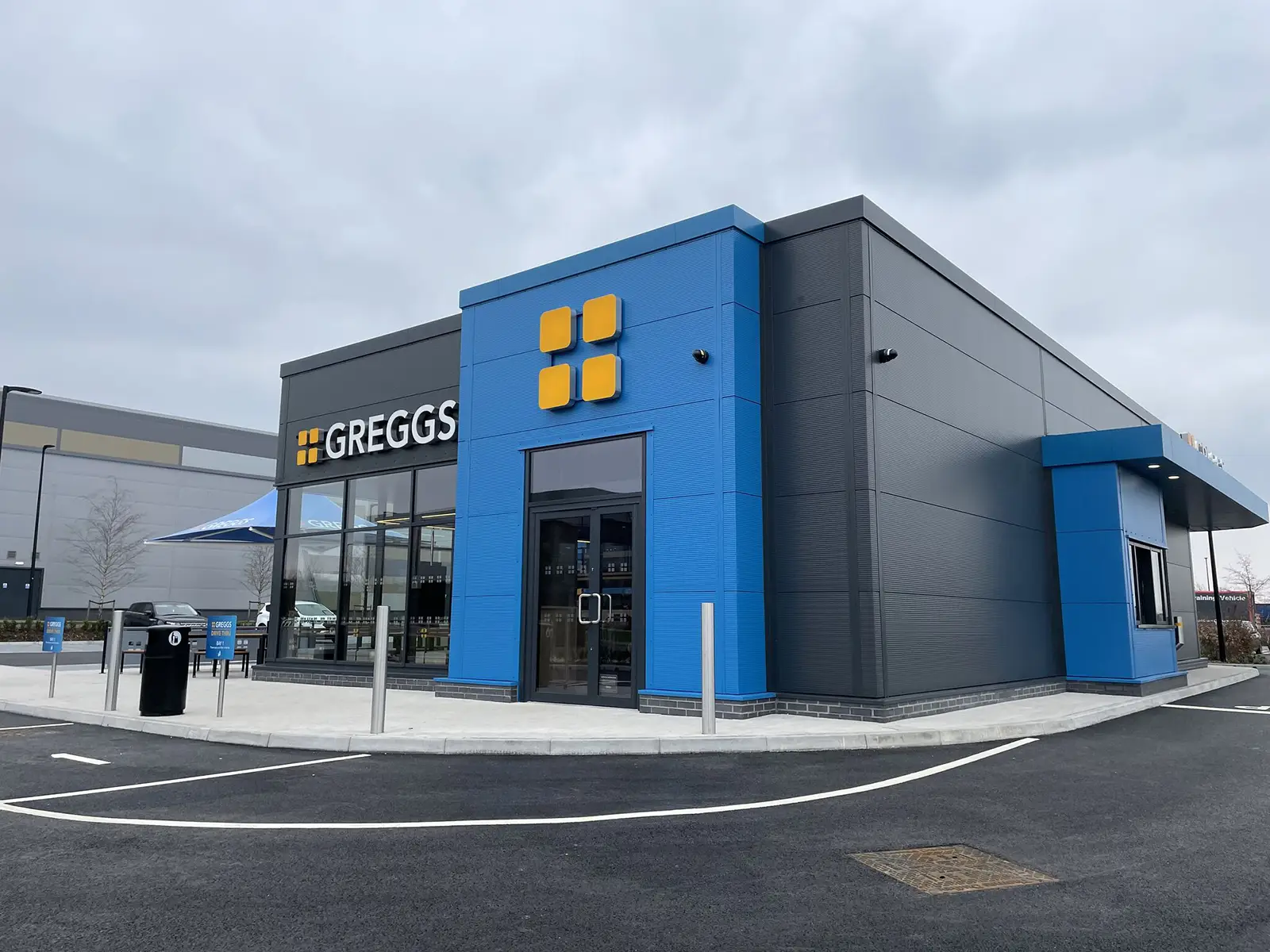 A modern Greggs store with blue and gray exterior and large glass windows.