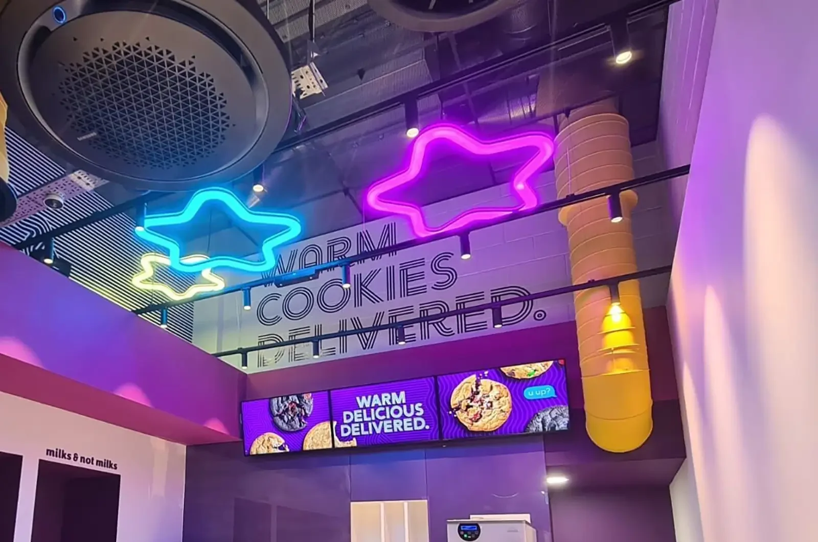 Neon star lights and "Warm Cookies Delivered" sign inside a modern, colorful store interior.