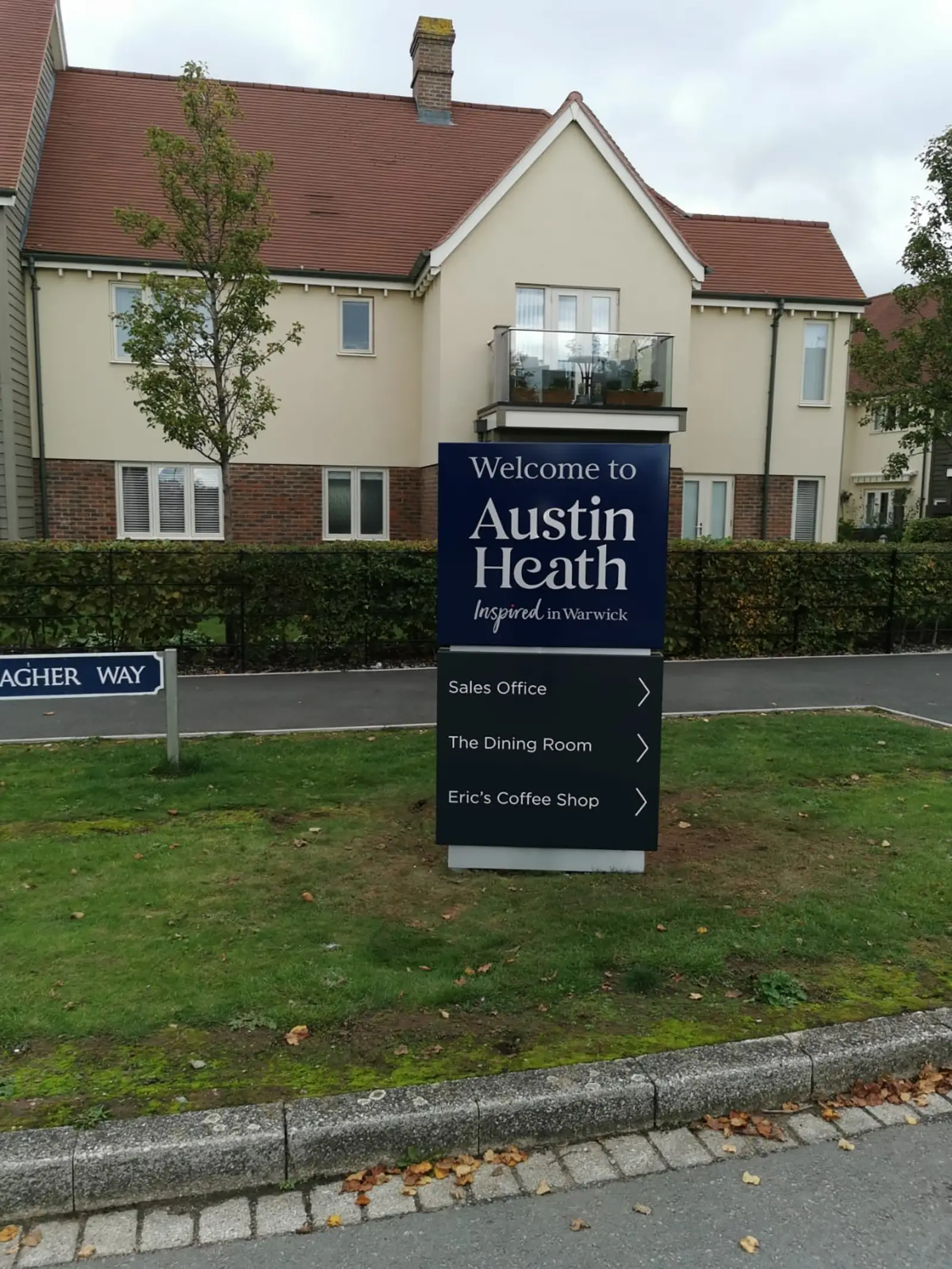 Sign for Austin Heath with directions, in front of residential buildings and trees.