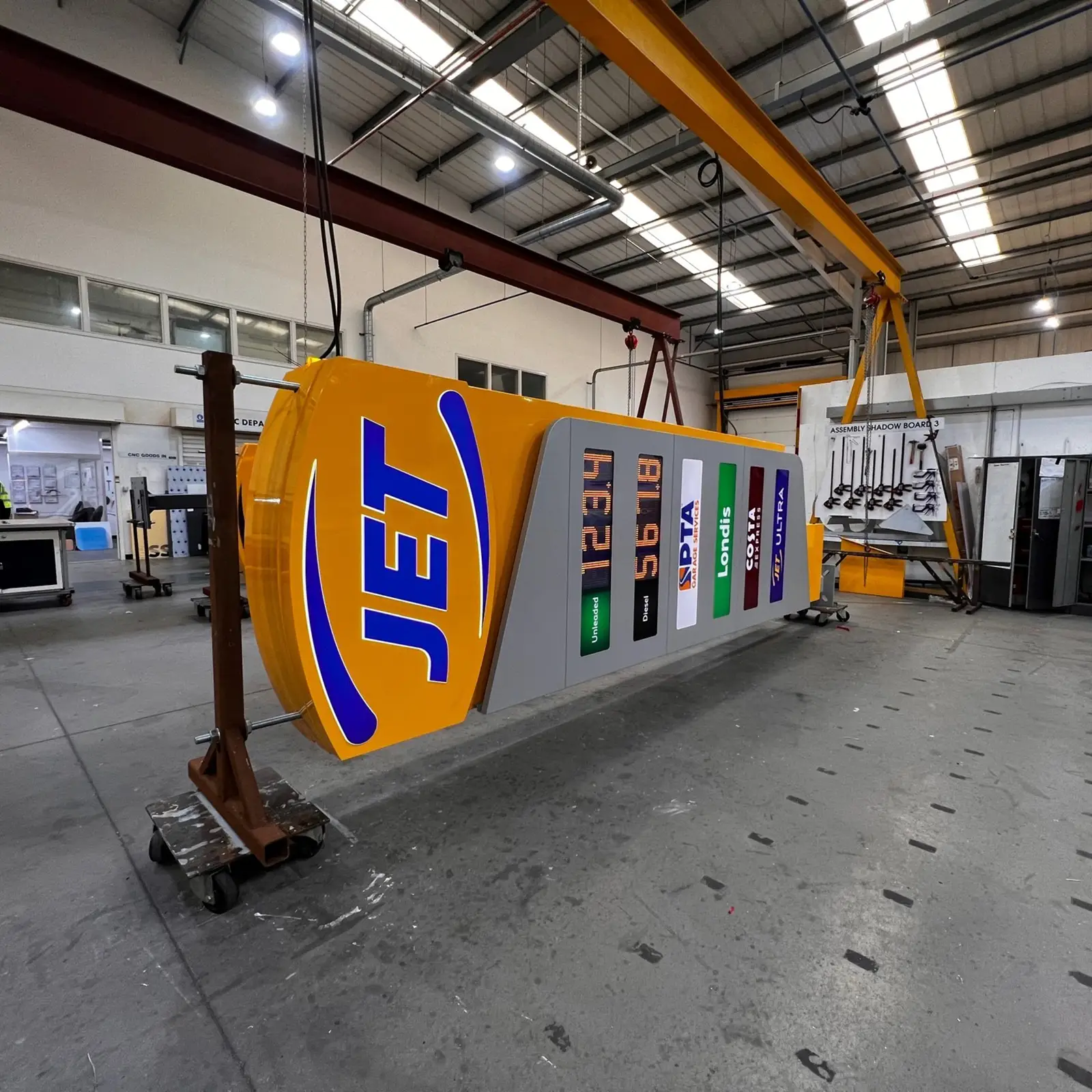 Large "JET" fuel station sign hanging from a yellow crane inside an industrial warehouse.