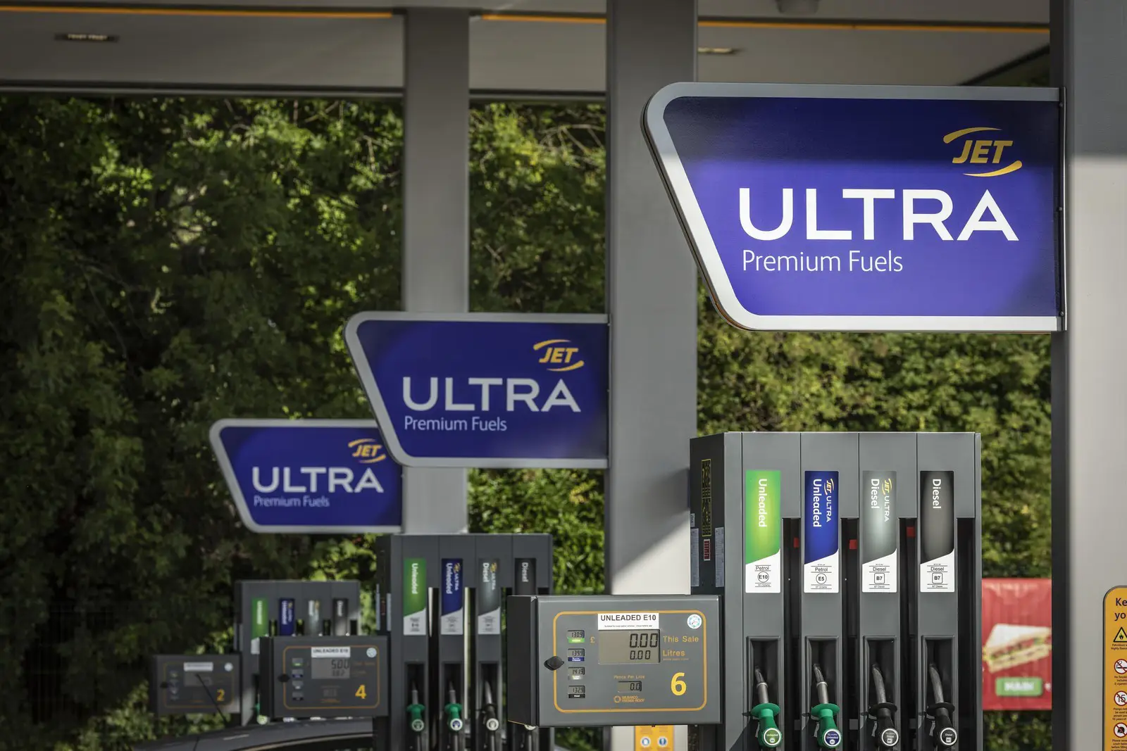 Gas station with multiple fuel pumps and signs reading "JET ULTRA Premium Fuels" against greenery.