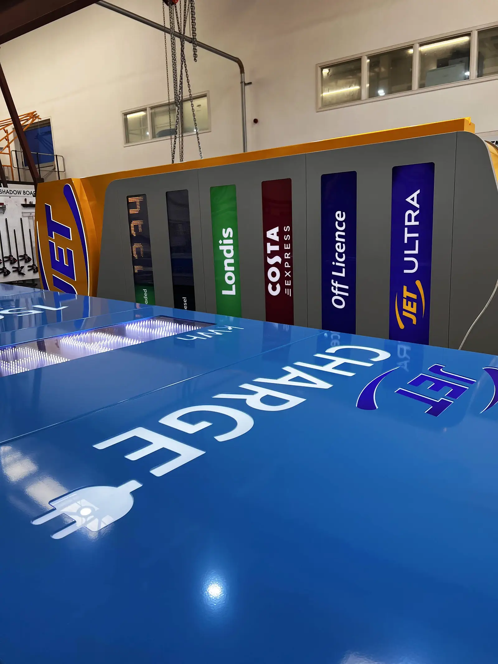 Blue electric vehicle charging station with a large sign and colorful vertical panels behind.