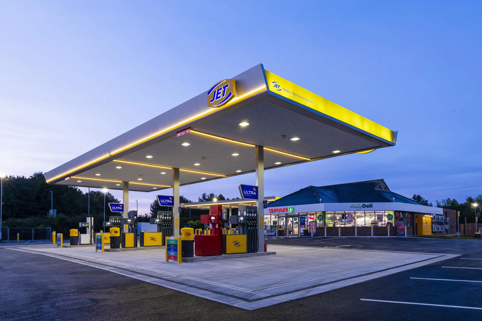 A well-lit gas station with a convenience store in the background during twilight.