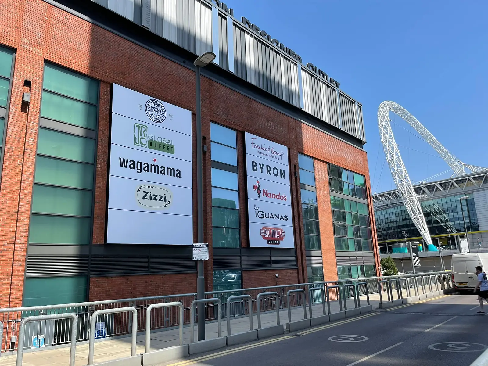 Red brick building with restaurant signs, including Wagamama and Nando's, near a stadium arch.