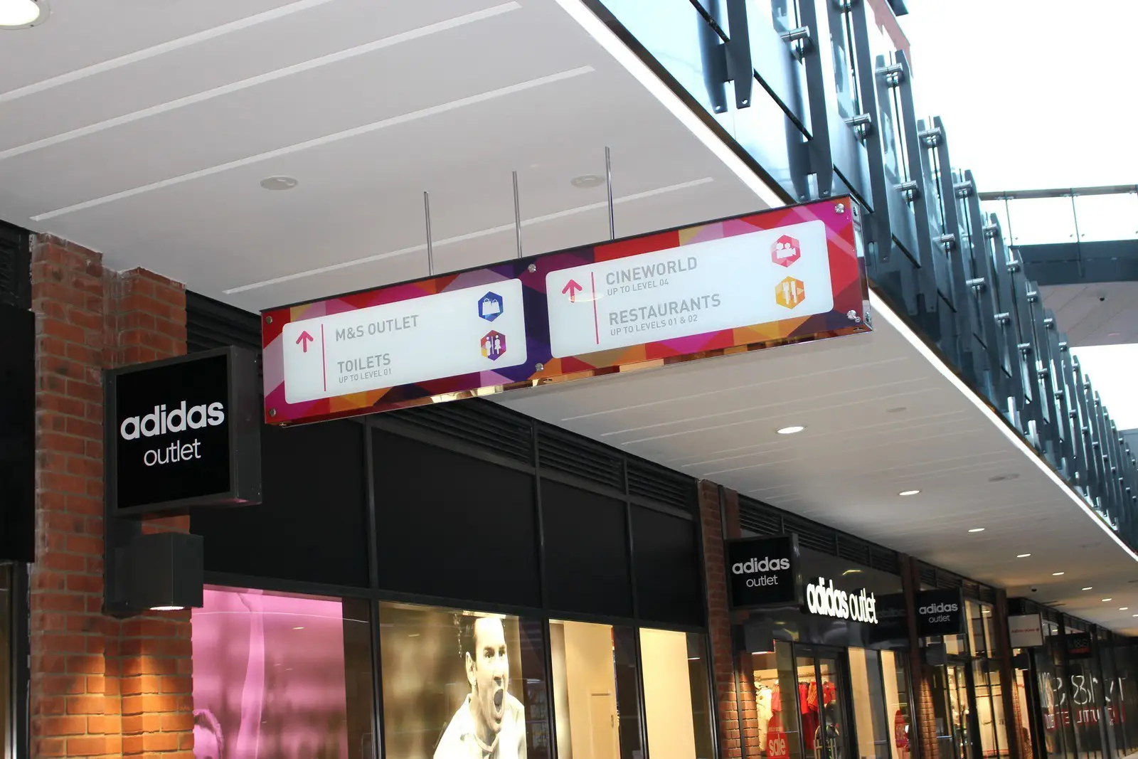 Shopping mall corridor with Adidas outlet and overhead sign directing to various locations.