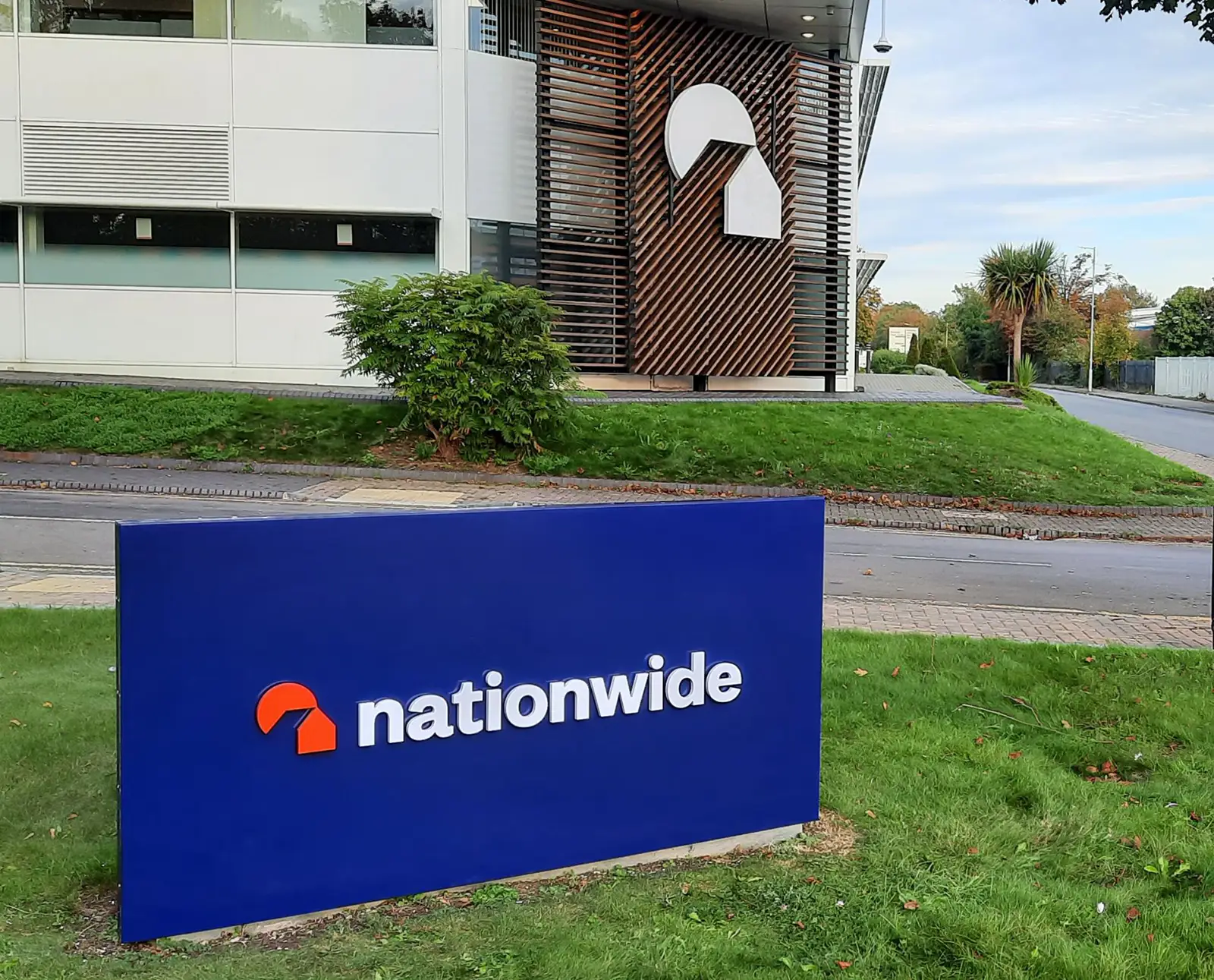 Blue sign with "nationwide" logo in front of a modern building with similar logo.