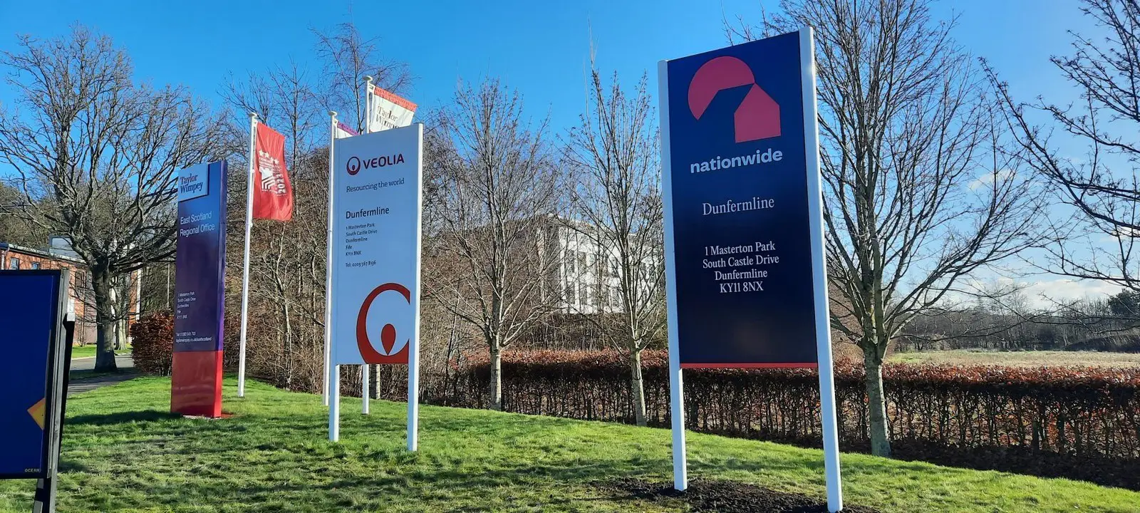 Several company signs on a grassy area with bare trees and a clear blue sky.