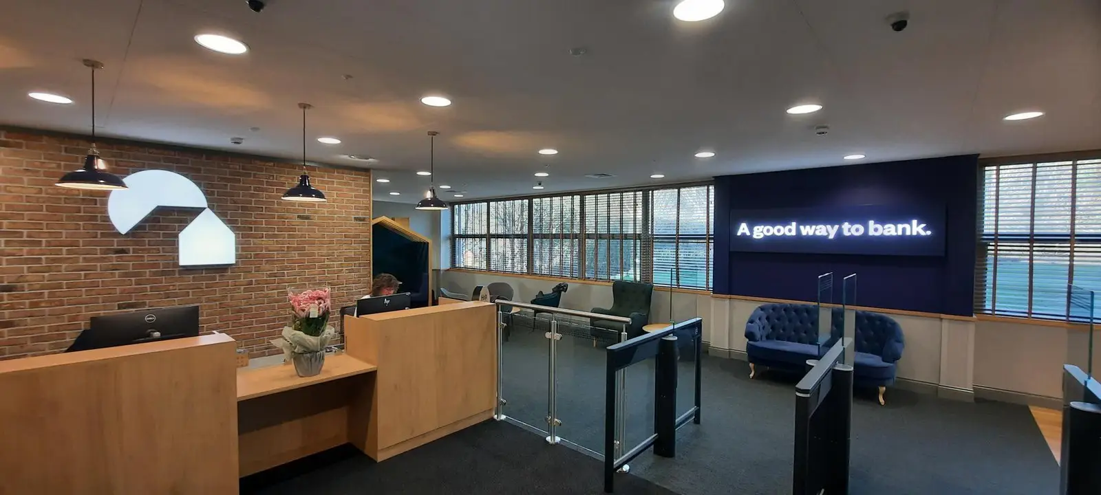 Modern bank interior with a reception desk, seating area, and illuminated sign on the wall.