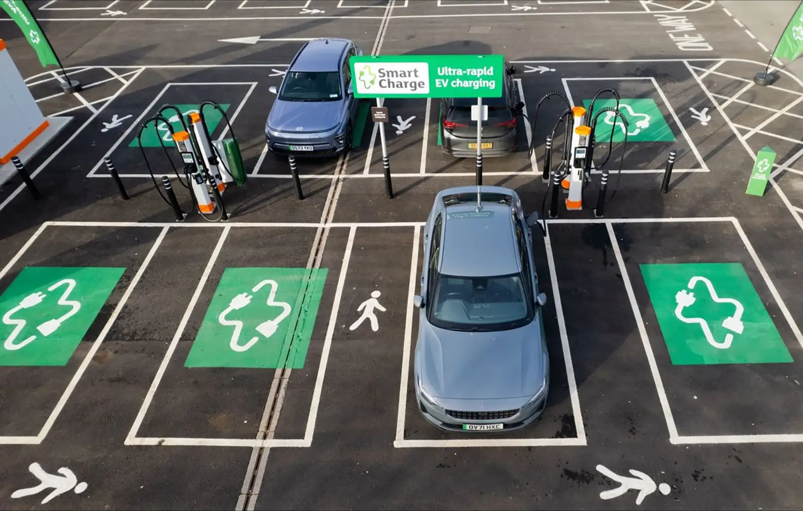 Cars parked at an electric vehicle charging station with green EV symbols on the ground.