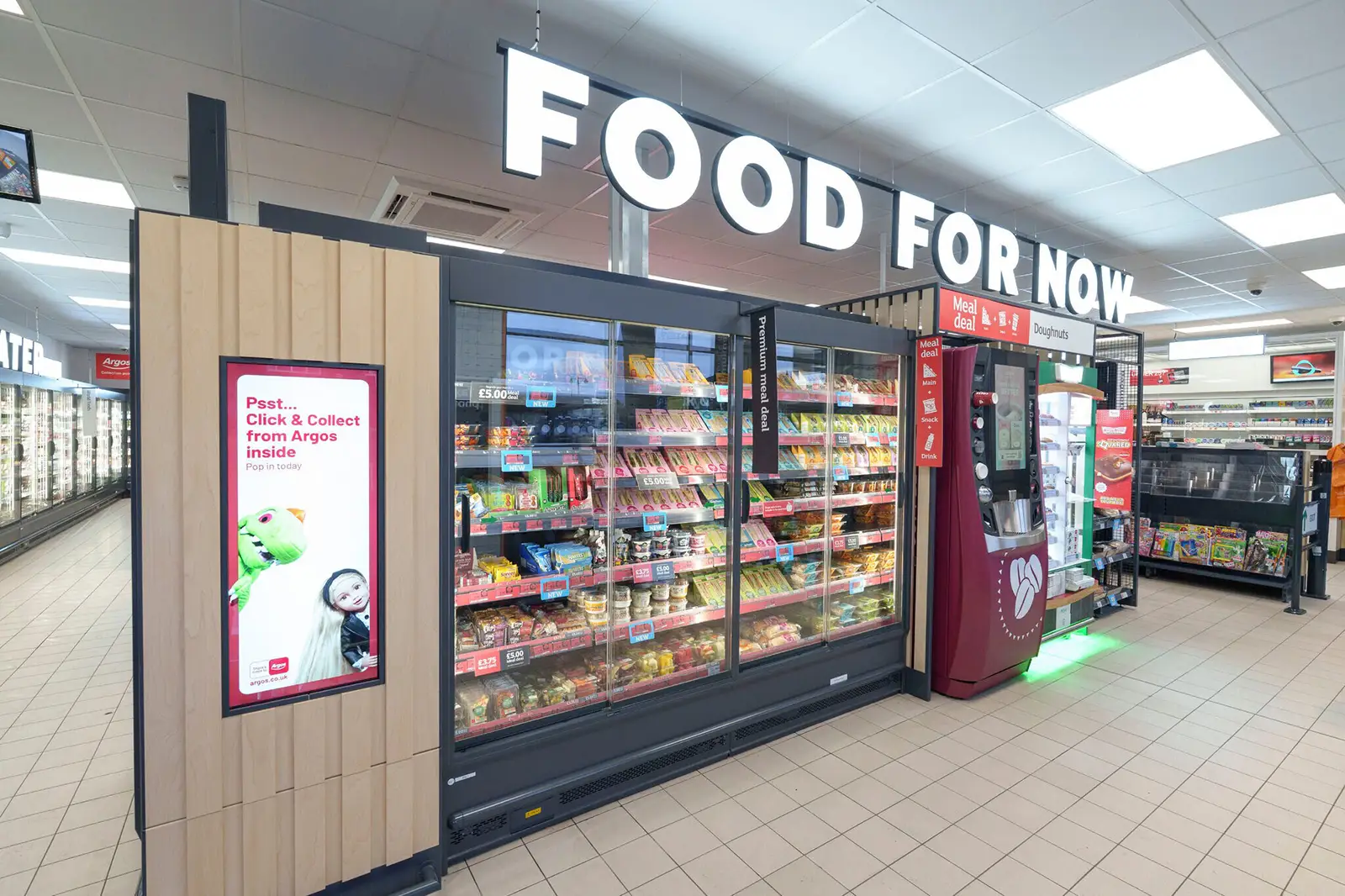 Supermarket aisle with refrigerated food display, digital kiosk, and large "FOOD FOR NOW" sign overhead.