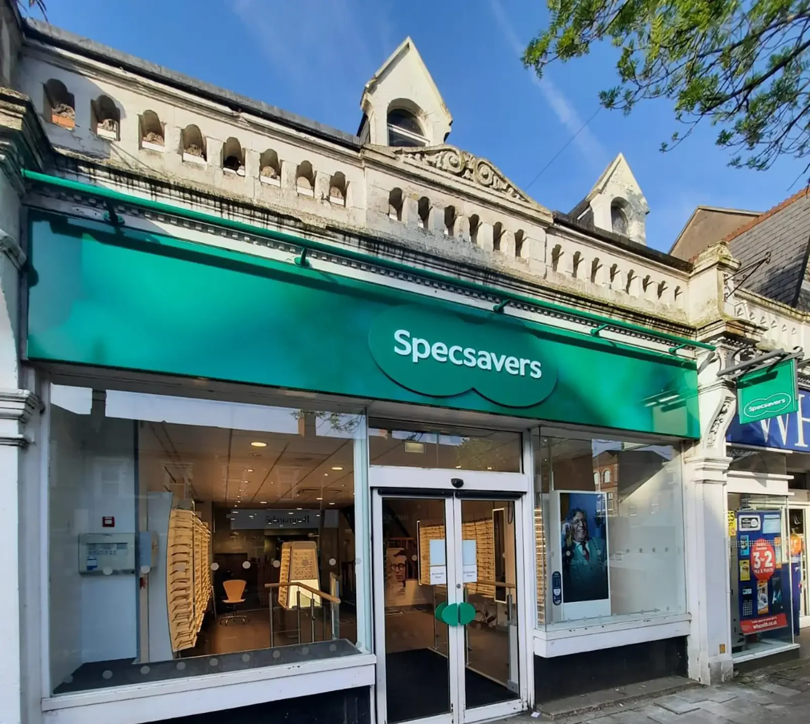 A Specsavers store with a green sign is located on a street with neighboring shops.