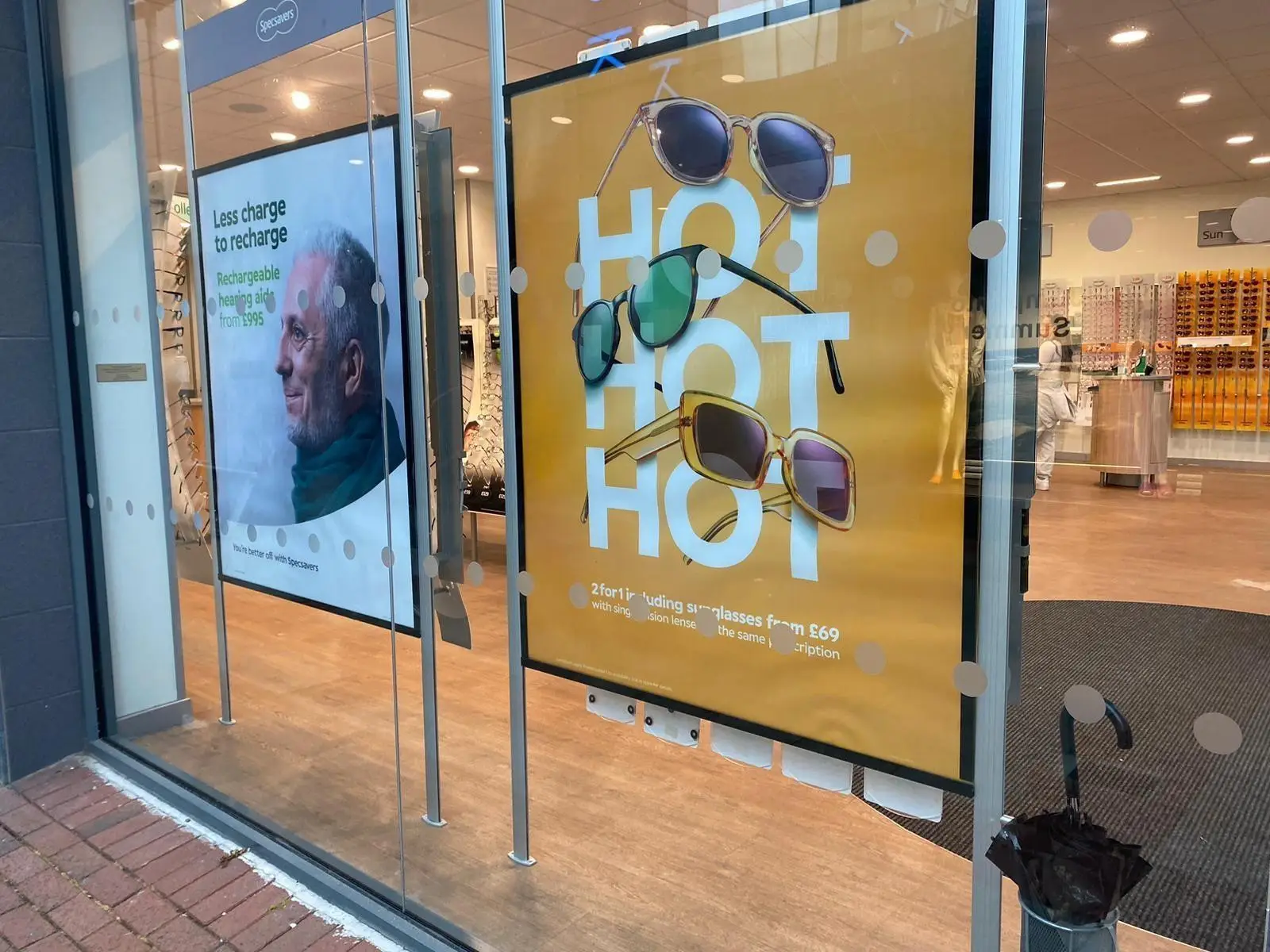Storefront with posters advertising sunglasses and a man with a green scarf inside.