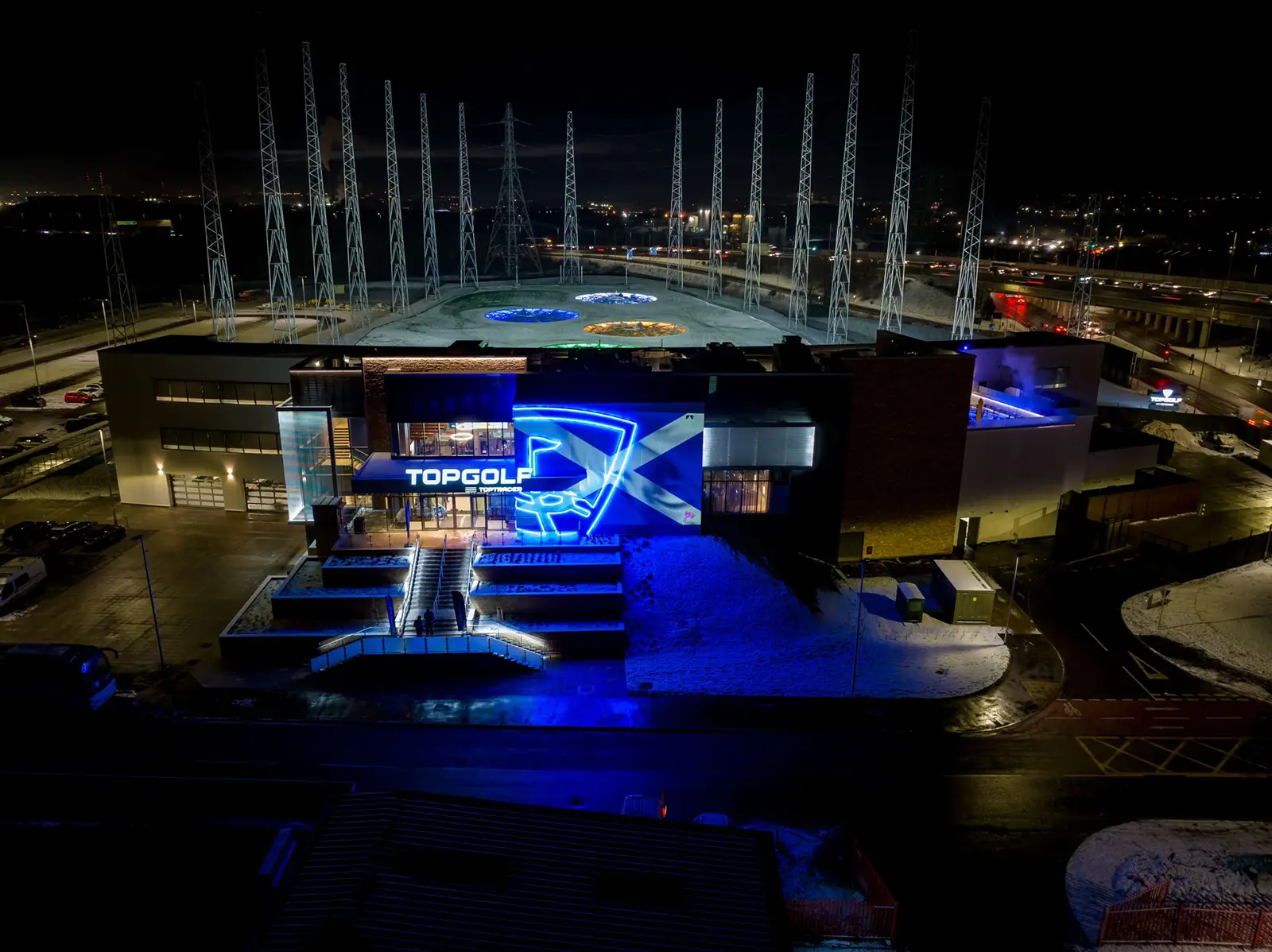 Aerial view of a Topgolf facility illuminated with blue lights at night.