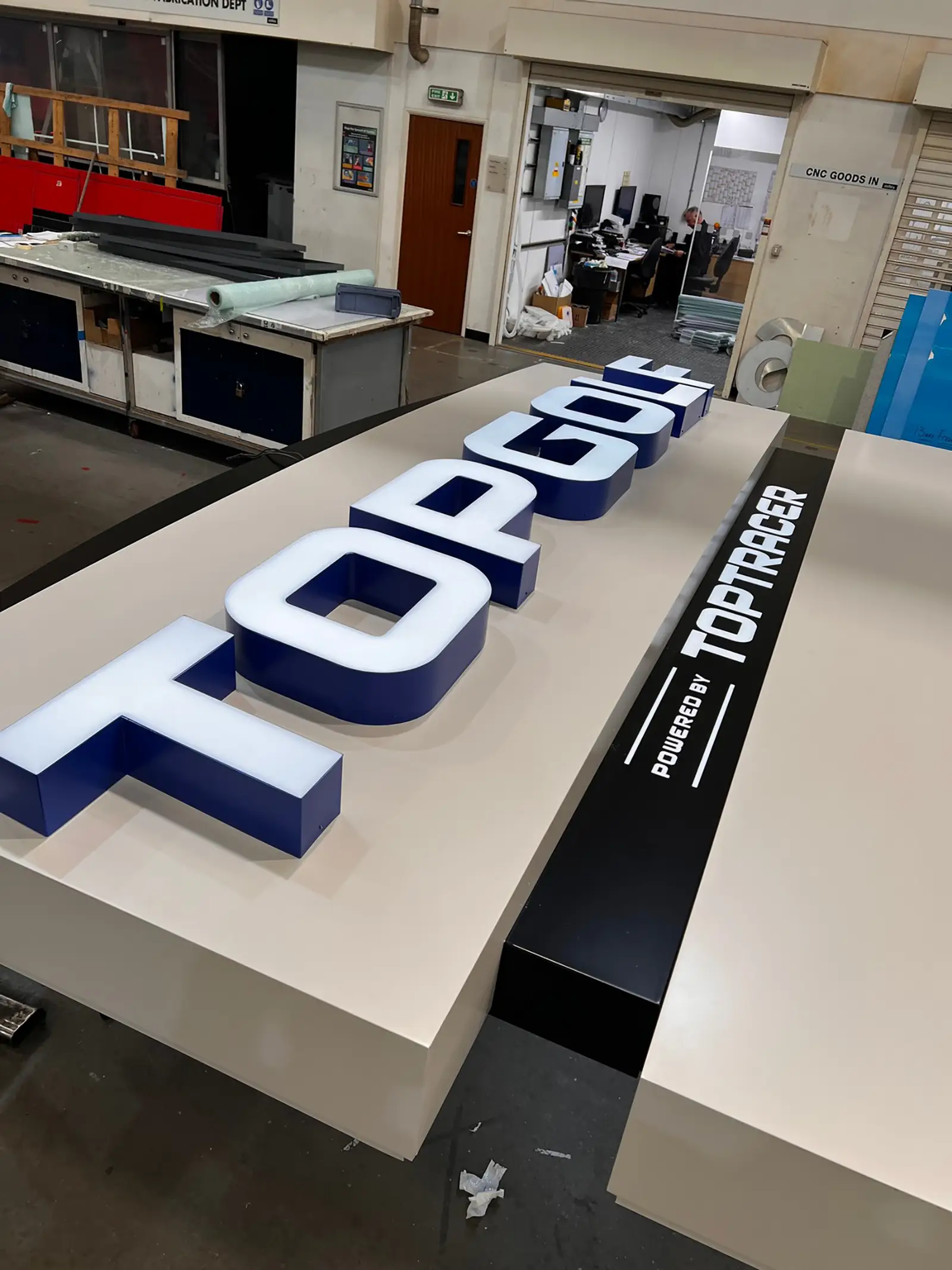 Large 3D "TOPGOLF" sign with "Powered by Toptracer" on a workshop table.