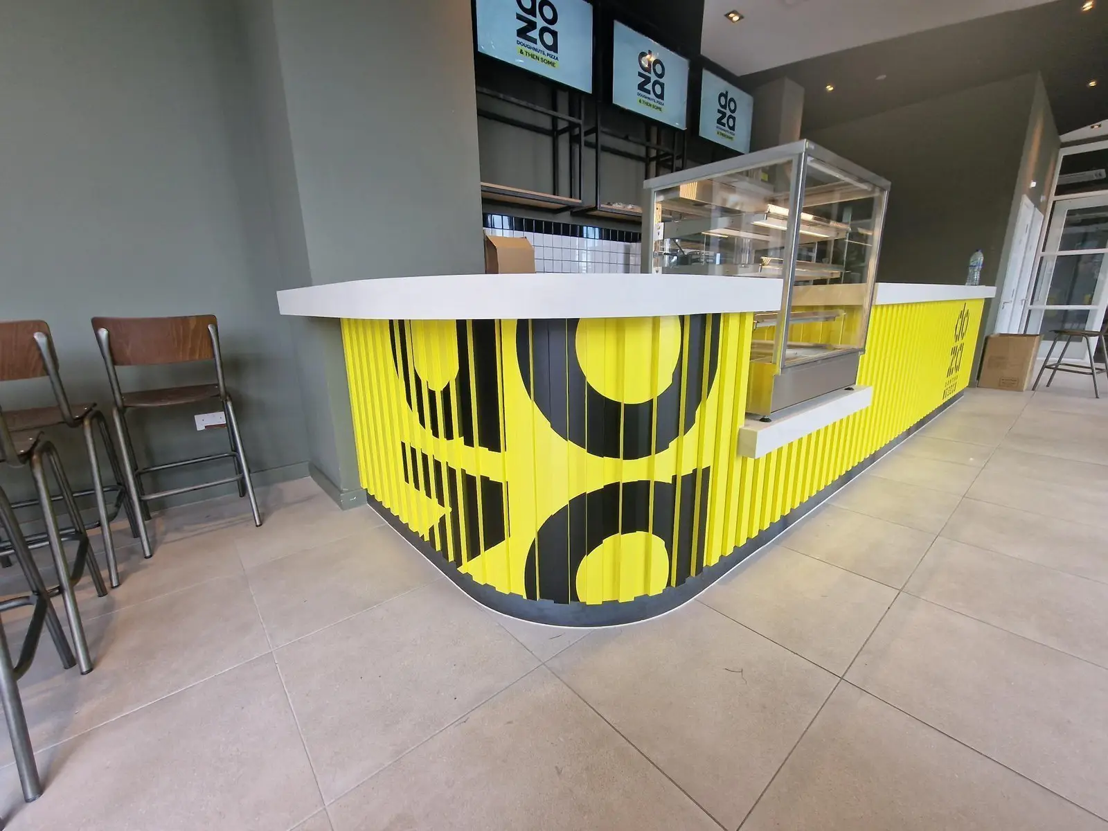A modern cafe counter with a yellow and black geometric design and empty display case.