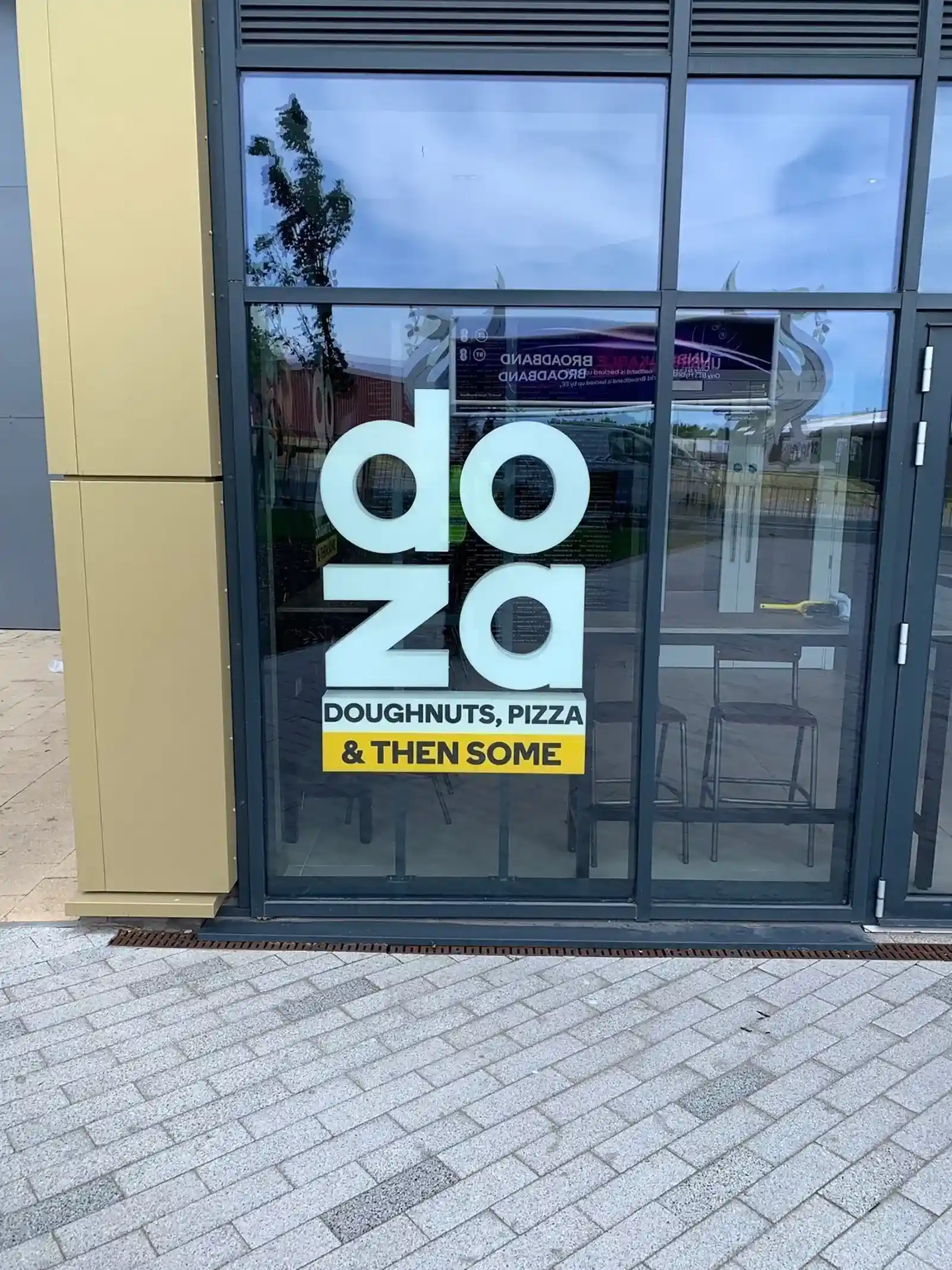 Glass door with "doza" and "Doughnuts, Pizza & Then Some" written in bold letters.