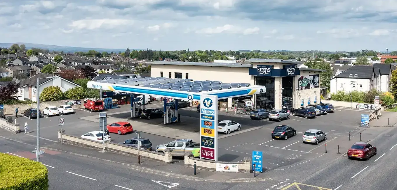 A gas station with multiple cars is situated at a busy intersection under a cloudy sky.