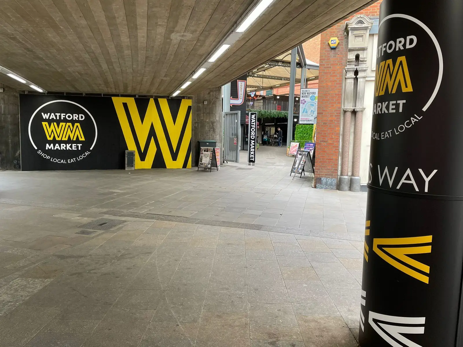 Entrance to Watford Market with large yellow and black signage under a concrete ceiling.