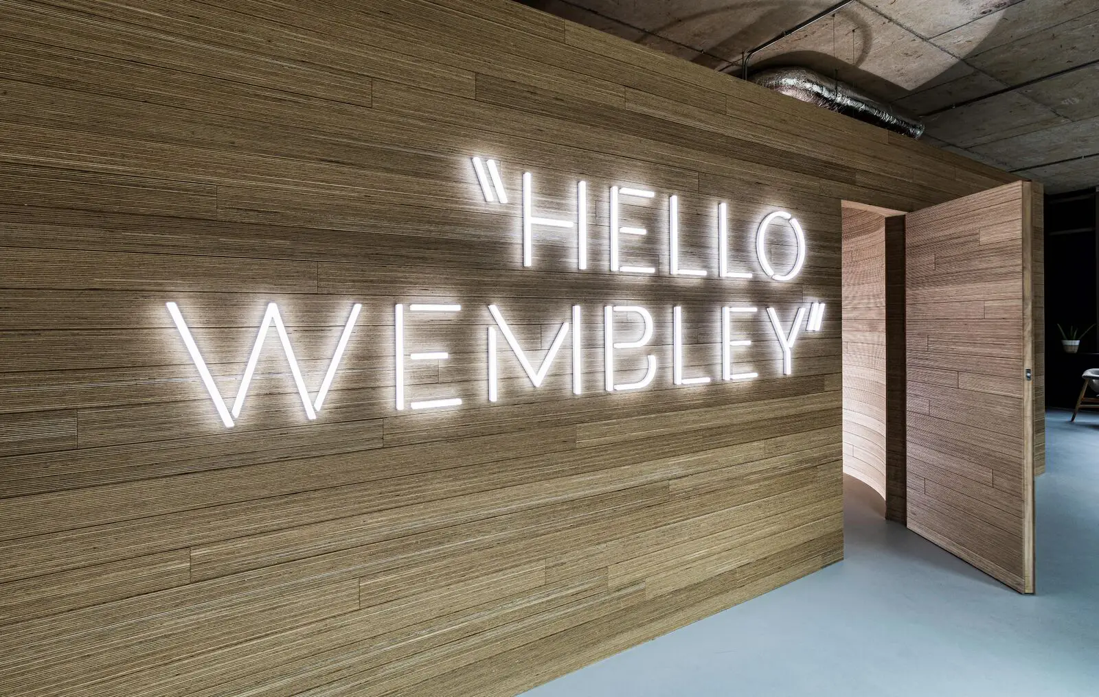 Illuminated "HELLO WEMBLEY" sign on a wooden wall with an open door nearby.