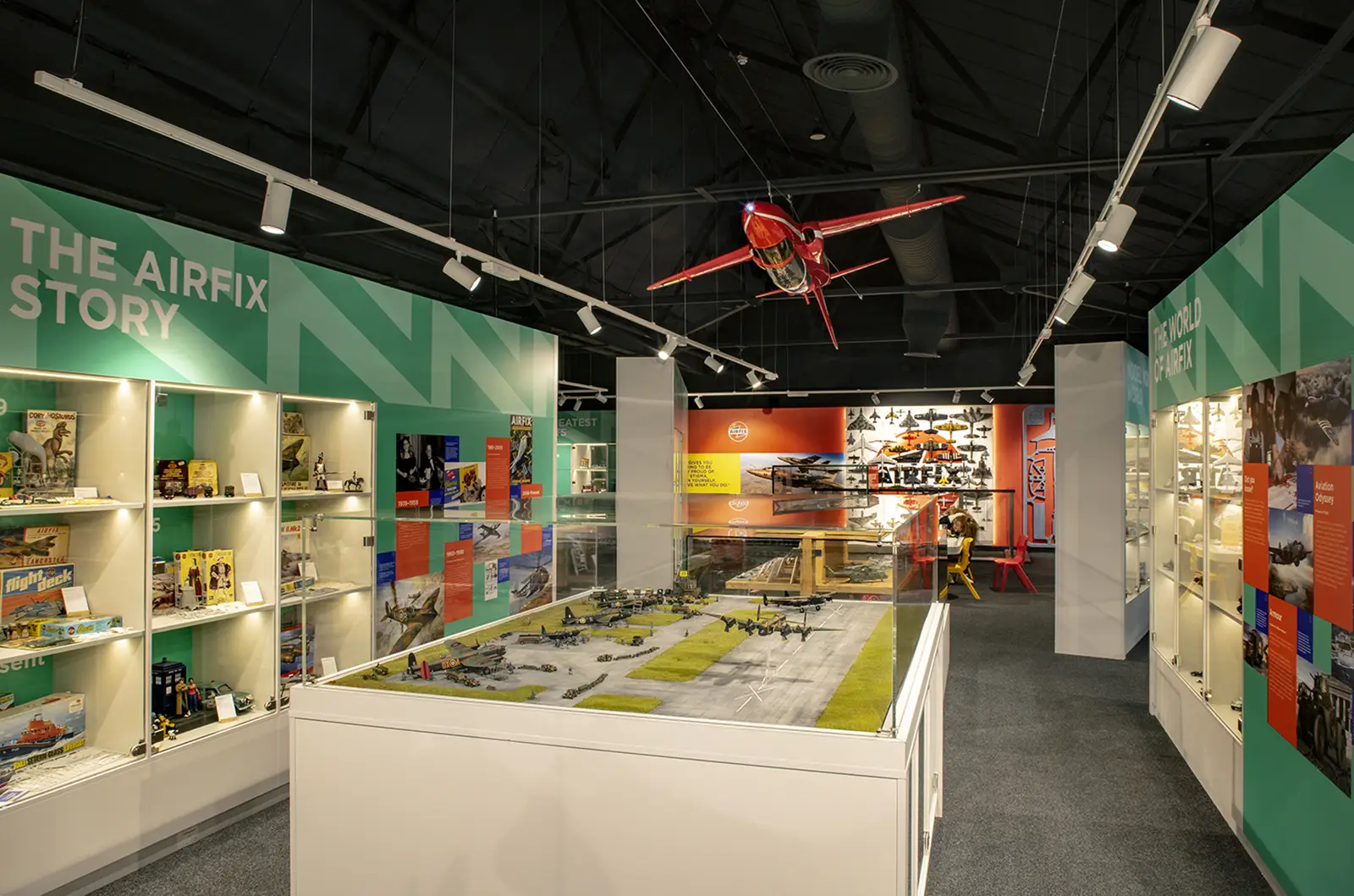 Museum exhibit with model airplanes, display cases, and a red plane suspended from the ceiling.