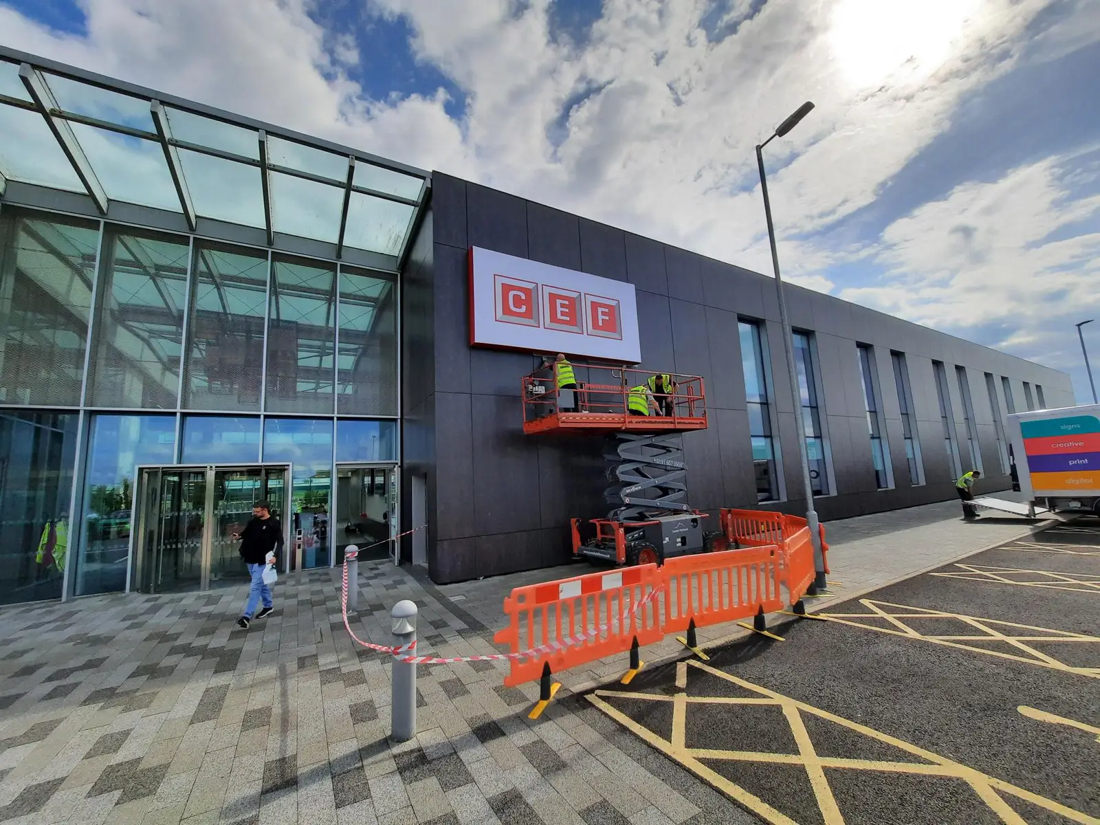 Workers on a lift installing a CEF sign on a modern building facade.