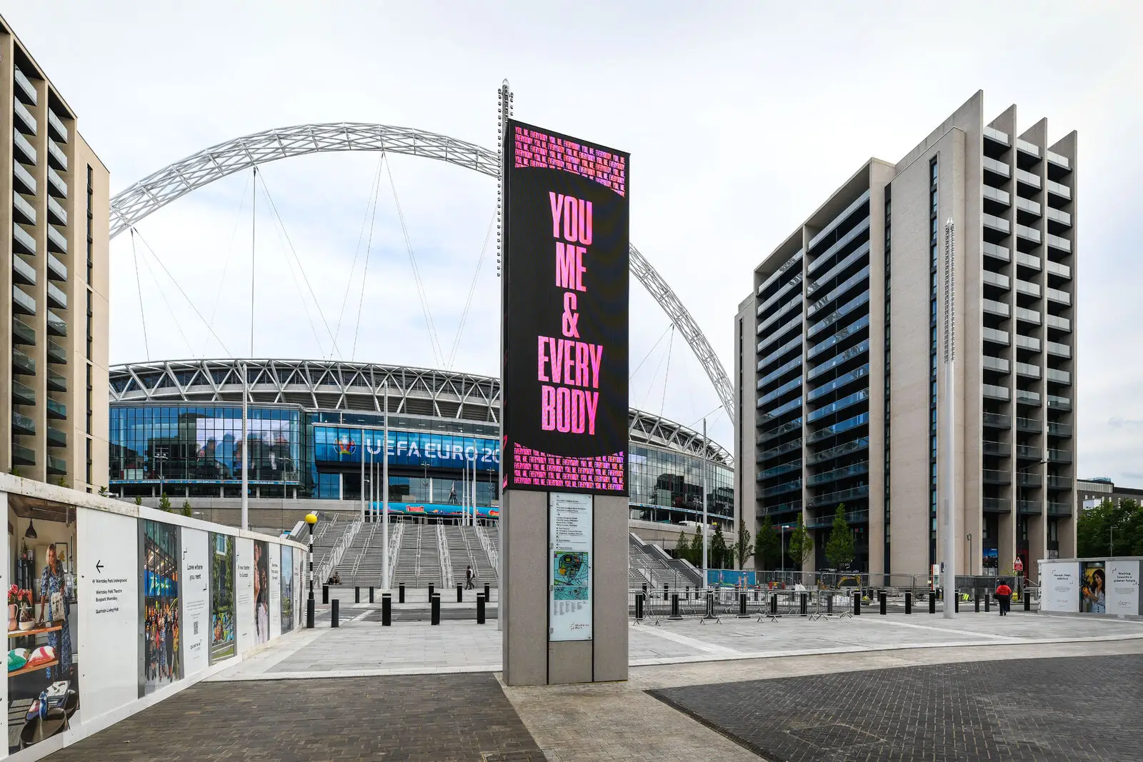 Wembley Stadium with a digital sign reading "YOU ME & EVERY BODY" in the foreground.