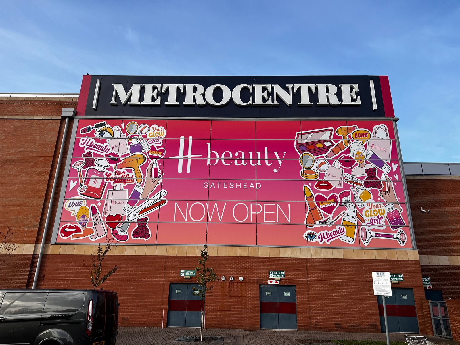 Large "METROCENTRE" sign above a colorful "H beauty GATESHEAD NOW OPEN" advertisement on a brick building.