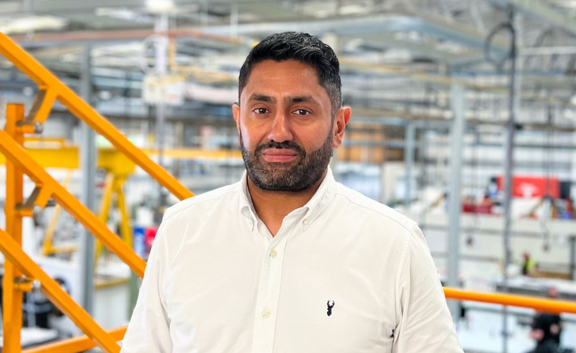 A person in a white shirt stands in an industrial setting with yellow stairs.