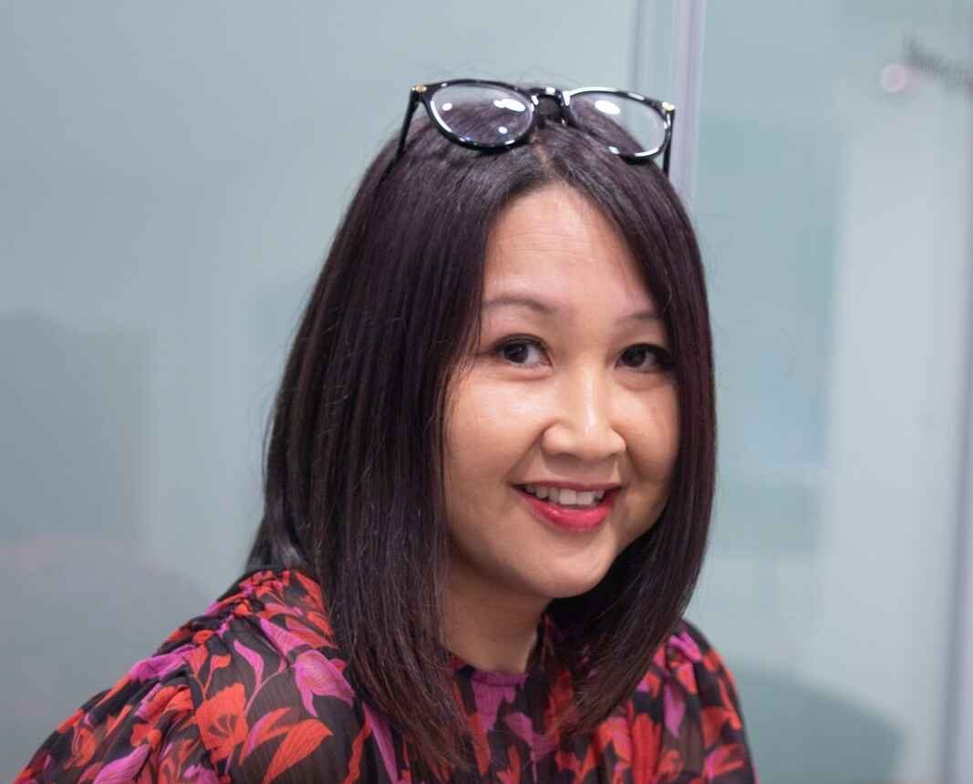 Woman with shoulder-length hair and glasses on her head, wearing a floral-patterned top.