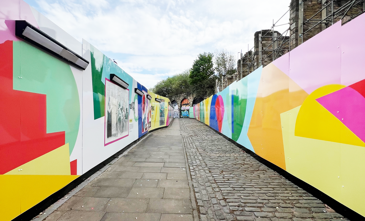 A narrow path lined with colorful geometric murals on both sides under a partly cloudy sky.