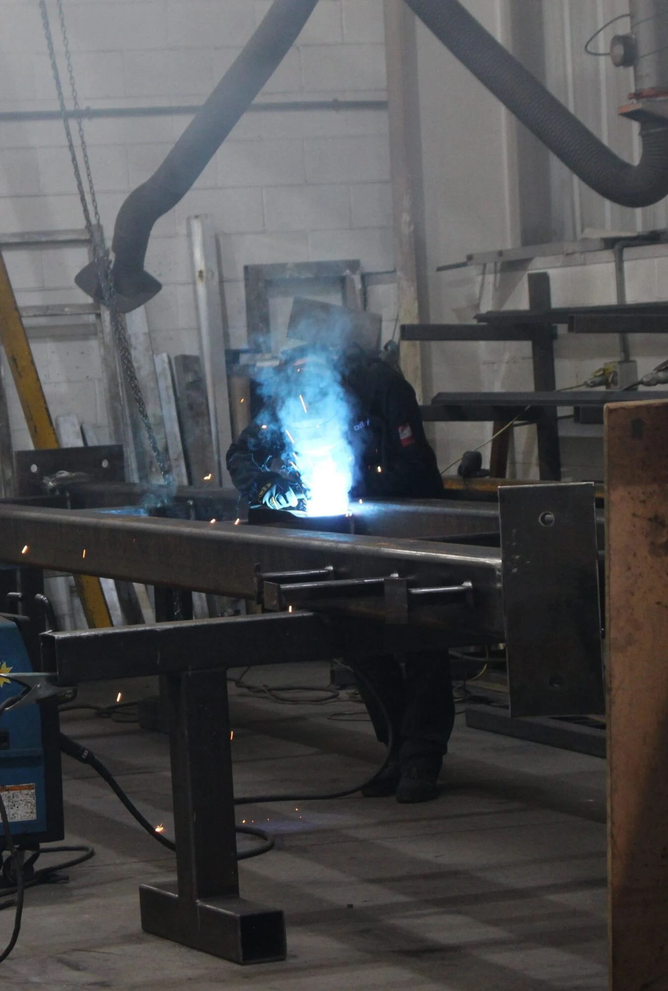 A person is welding a metal beam in an industrial workshop with bright sparks.