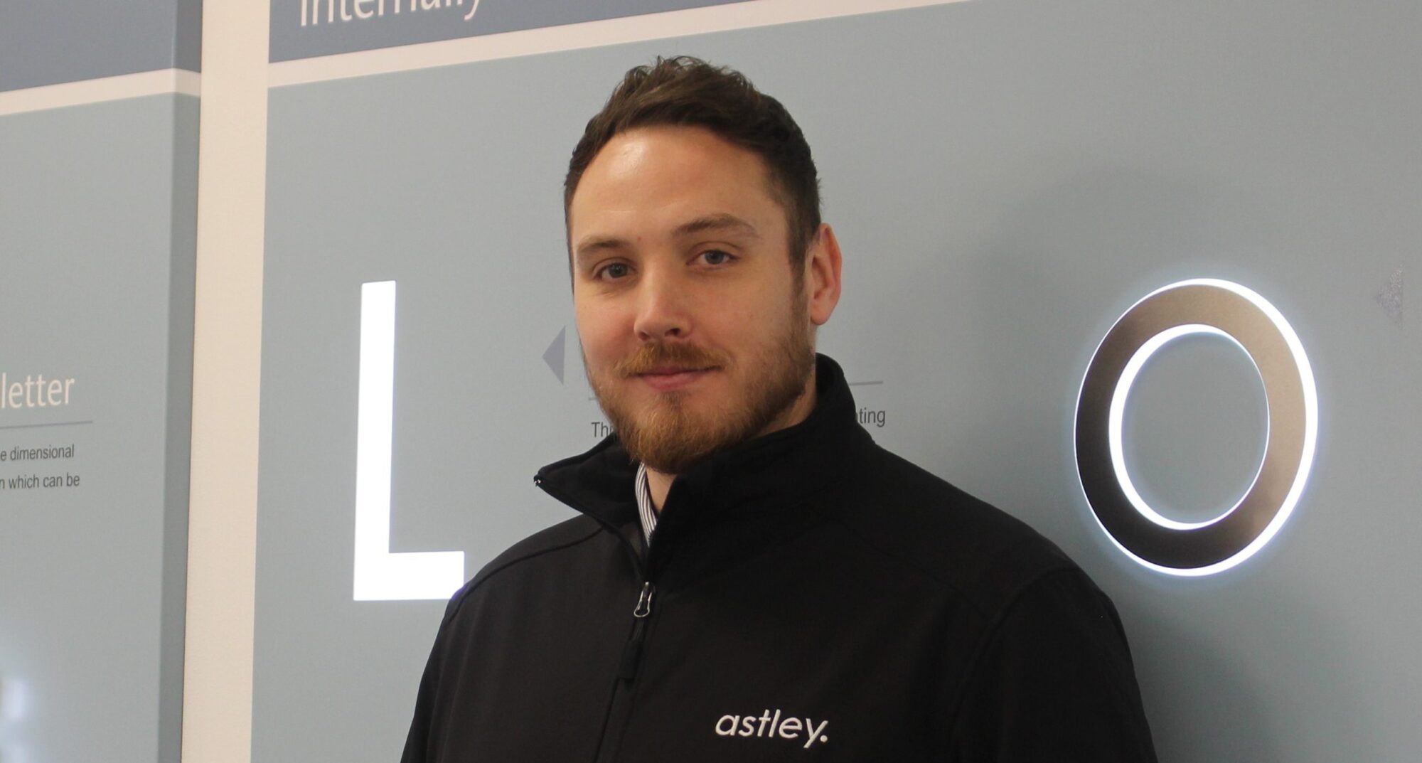 Man in a black jacket with "astley." logo stands in front of a blue wall.