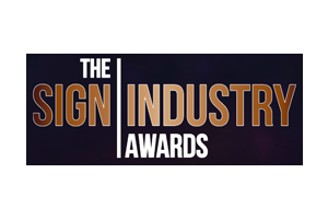 The Sign Industry Awards logo with bold white and brown text on a dark background.