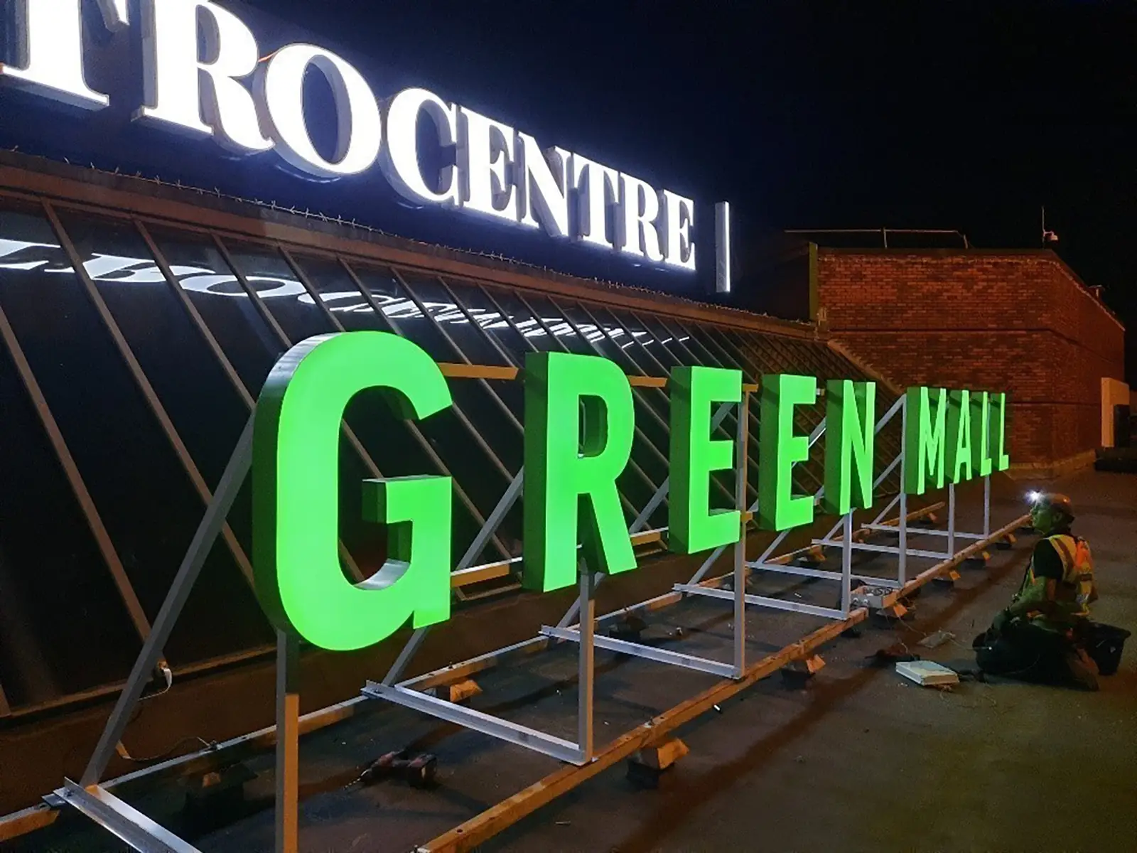 Large green "GREEN MALL" letters being installed on a rooftop at night.