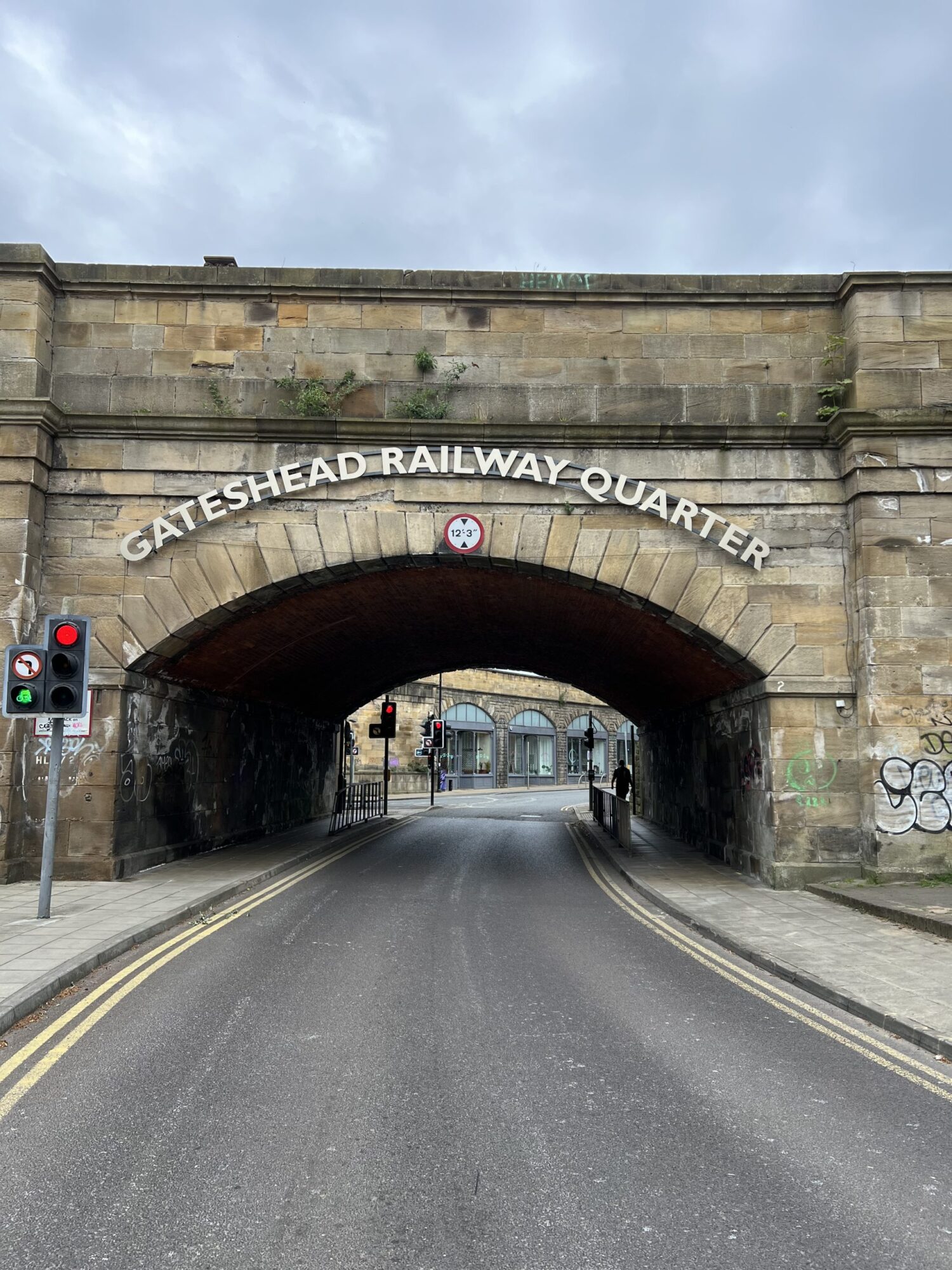 Stone railway bridge labeled "Gateshead Railway Quarter" with traffic lights and a road underneath.