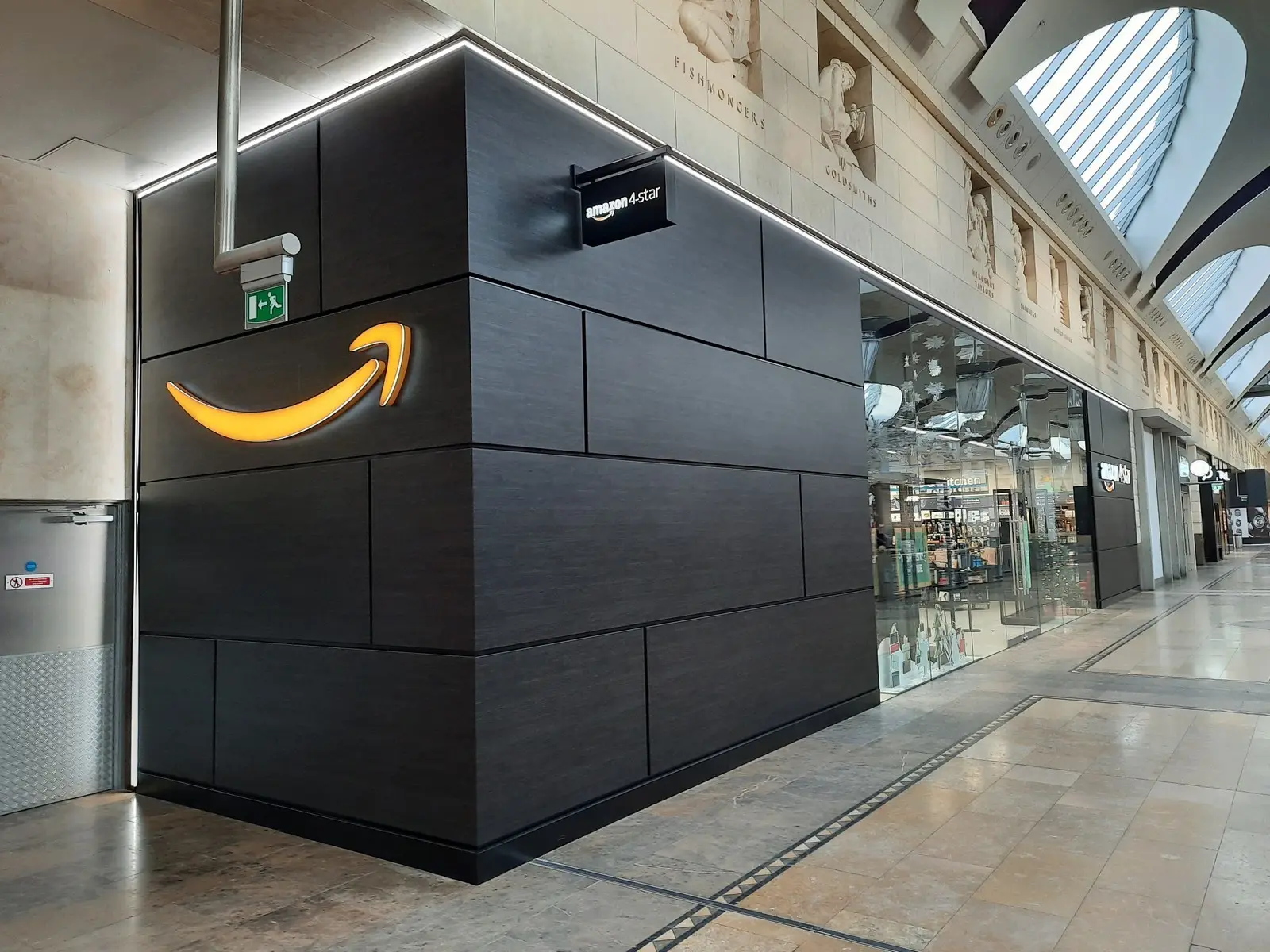 A dark storefront with an illuminated yellow arrow logo in a shopping mall corridor.