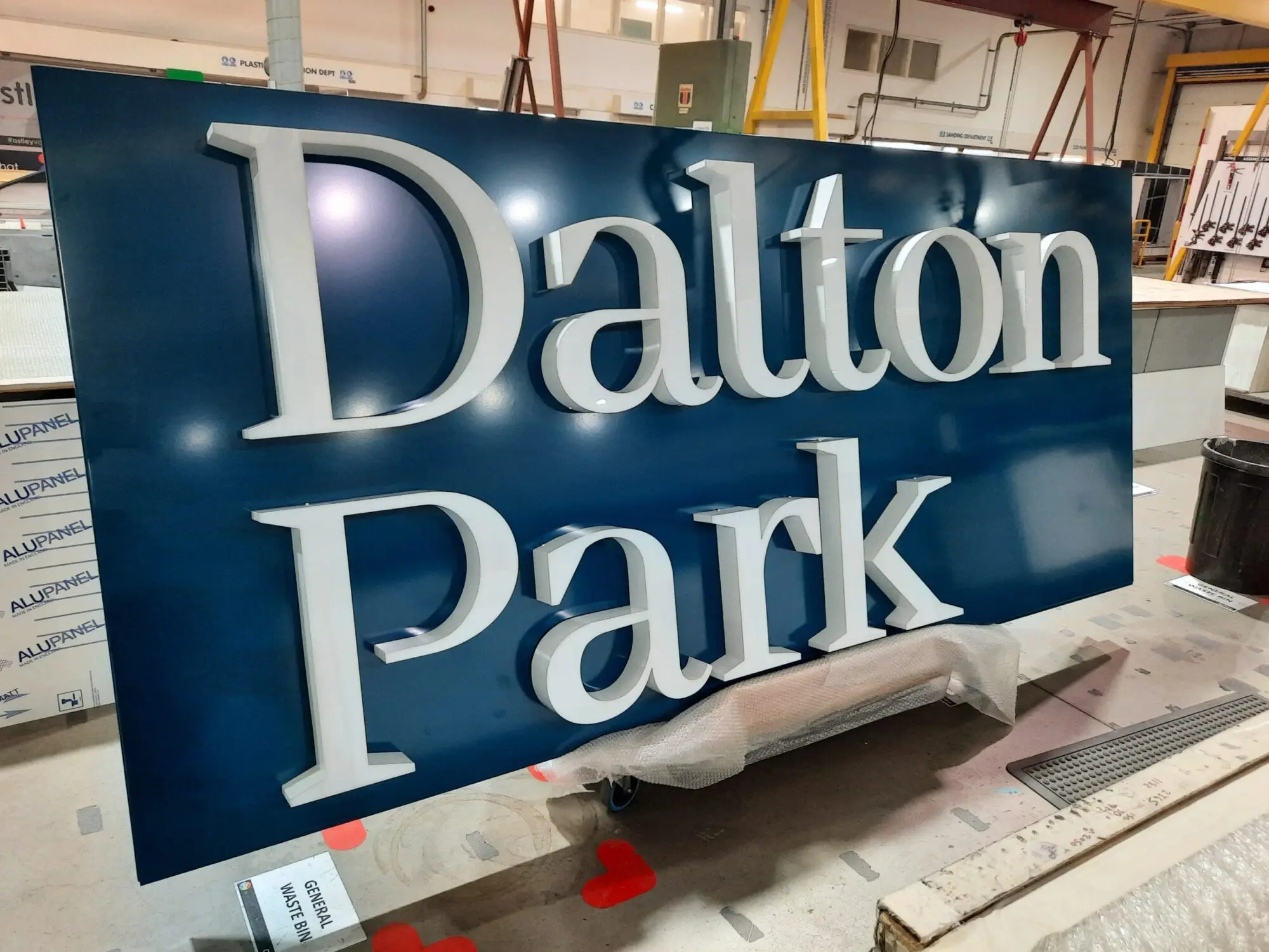 Large blue sign with raised white letters reading "Dalton Park" in a workshop setting.