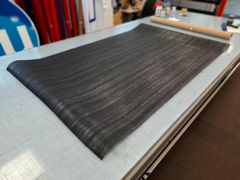 A large sheet of black carbon fiber fabric lies on a worktable in a workshop.
