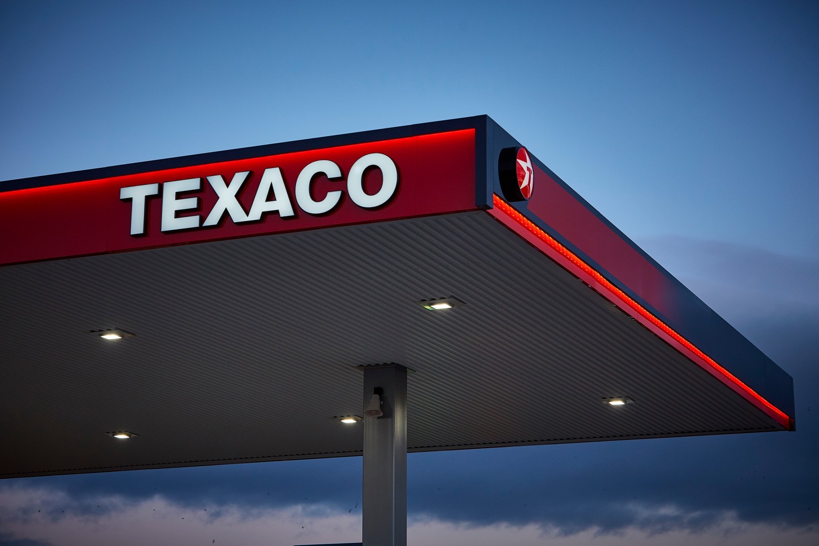 Texaco gas station canopy with illuminated red and white signage against a twilight sky.